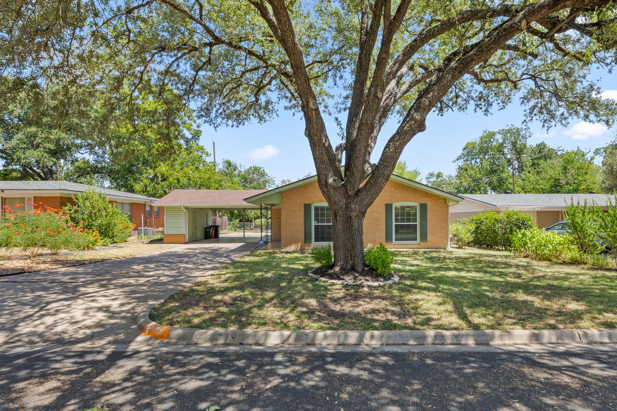 Mature shade trees frame the classic brick exteri