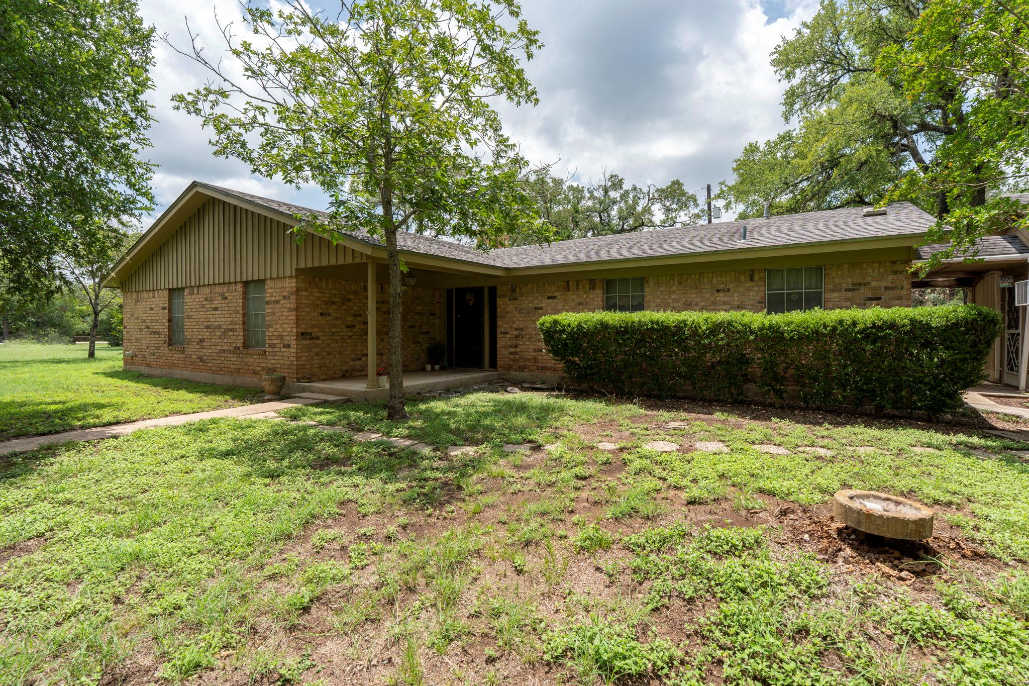 Back of house with brick siding, a lawn, and a pa