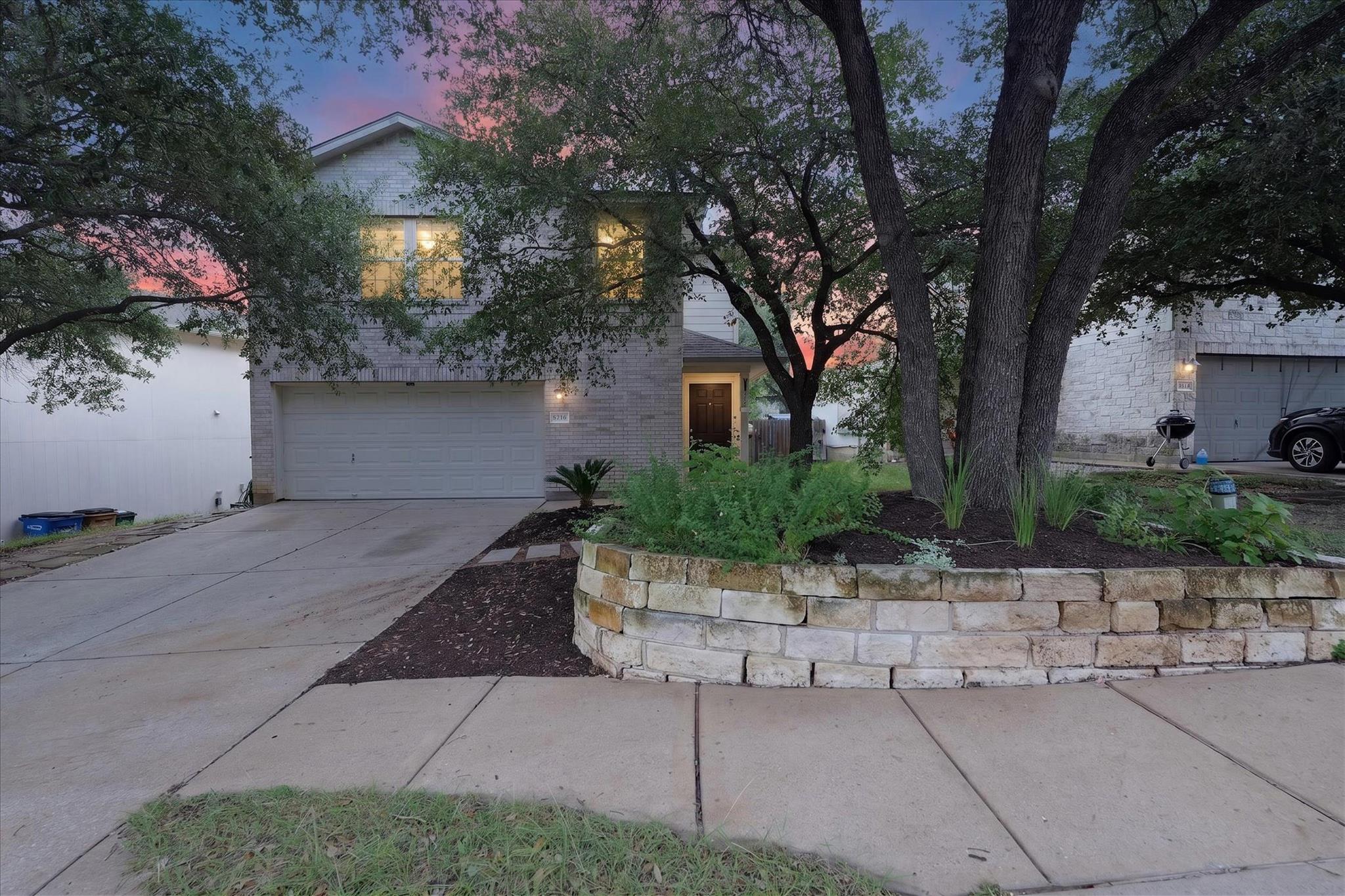 Mature trees and a stone-lined garden bed enhance