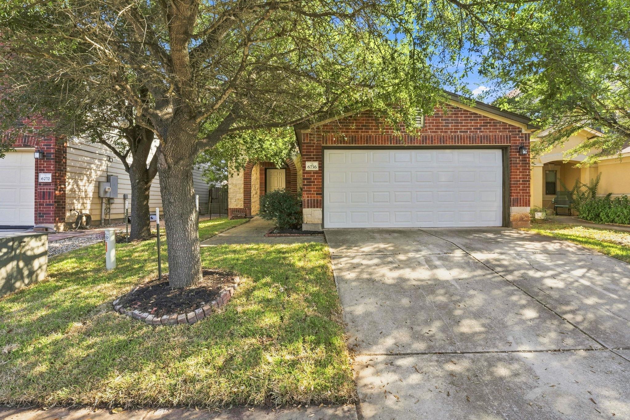 Mature trees shade the concrete driveway and bric