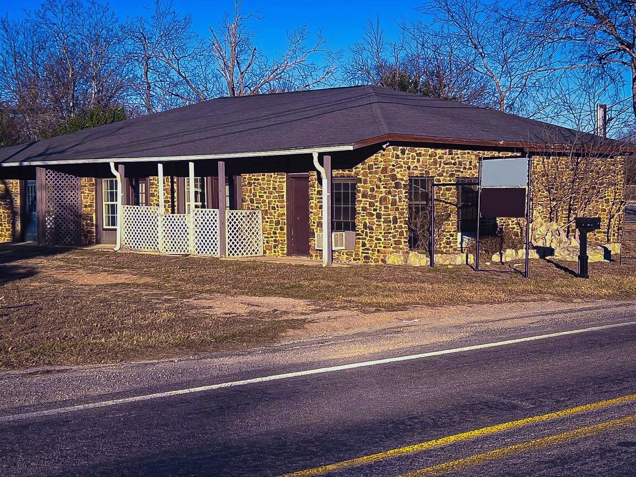 Stone exterior with a dark shingle roof and a cov