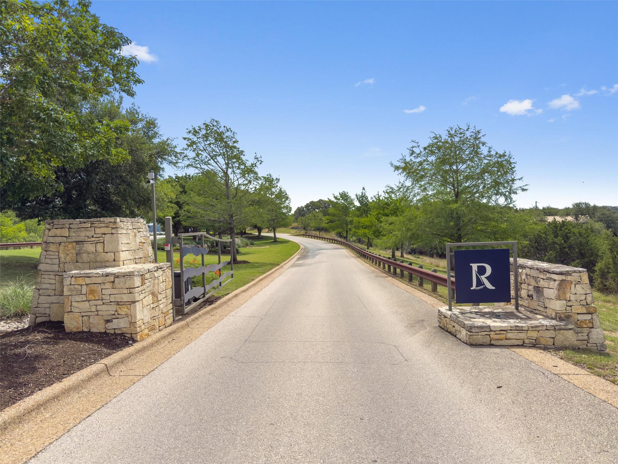 Stone entrance columns flank a paved driveway, fe