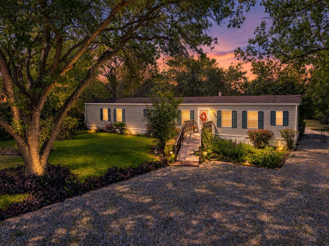 Mature trees frame a welcoming gravel driveway le