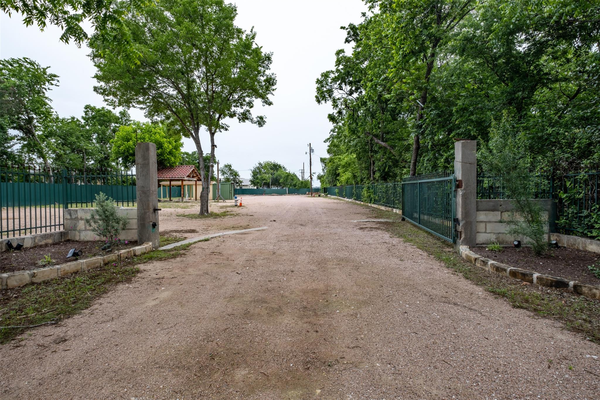 Gated entry with a gravel drive, bordered by matu