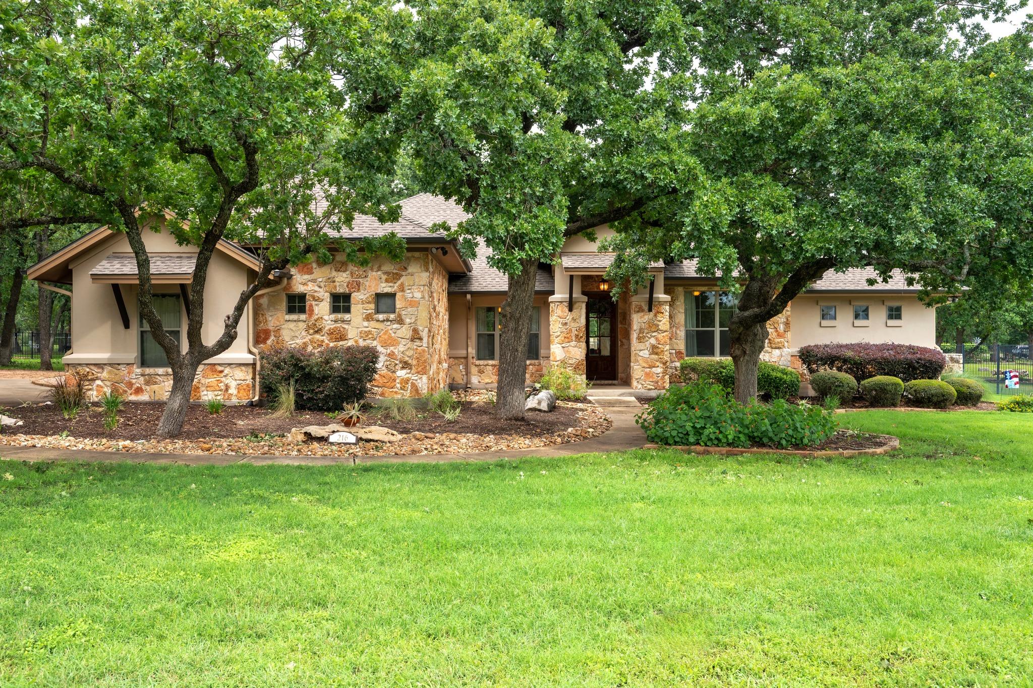 Stone and stucco exterior with multiple mature tr