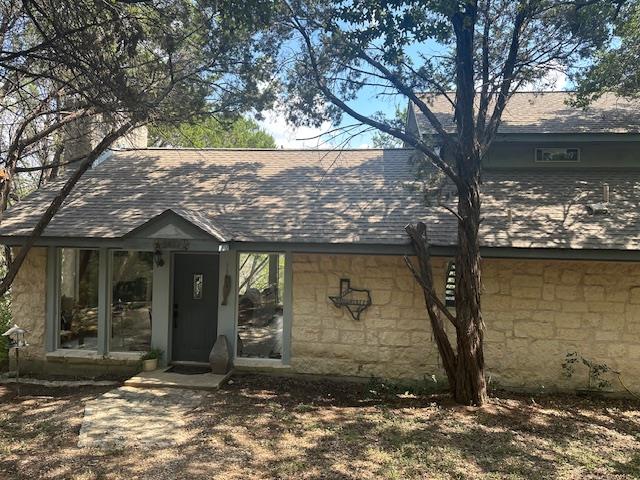 Stone veneer exterior with a grey shingle roof