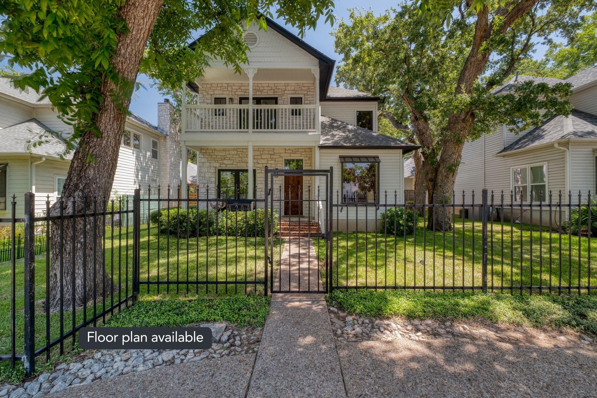 A charming home boasts an iron fence and mature t
