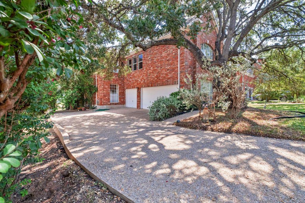Mature trees and a concrete driveway lead to a ch
