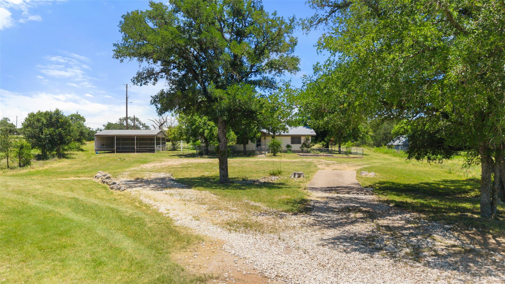 A gravel drive leads through mature trees to a se