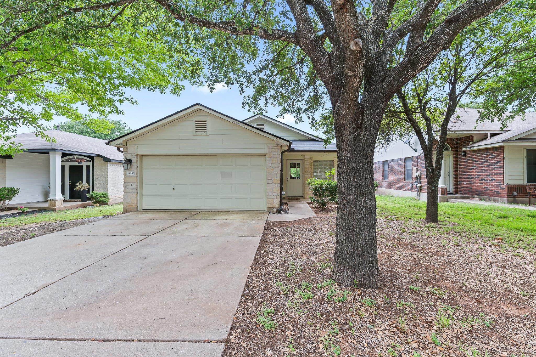A welcoming facade with mature trees, a driveway,