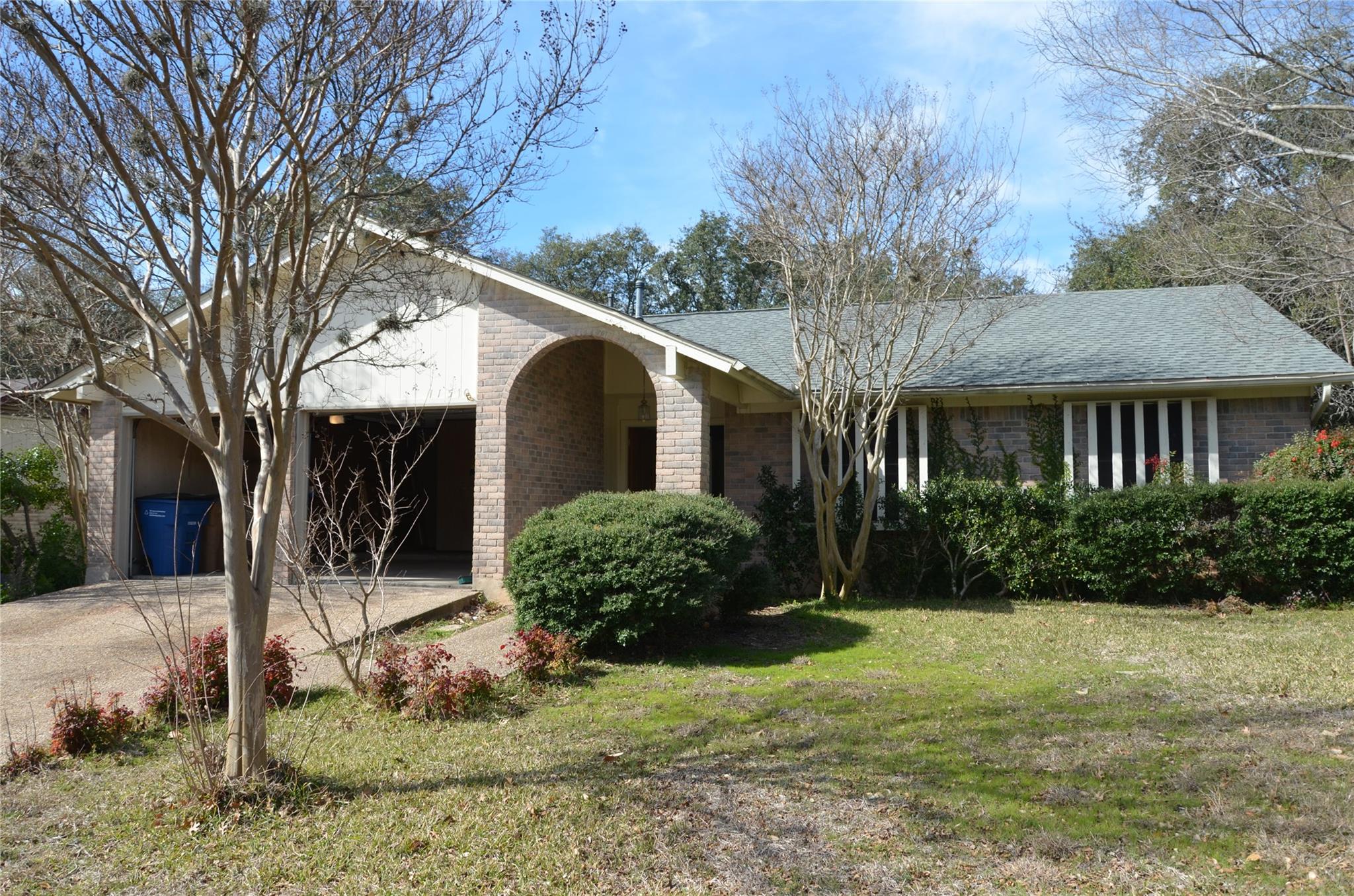 Mature trees frame a classic single-story brick f