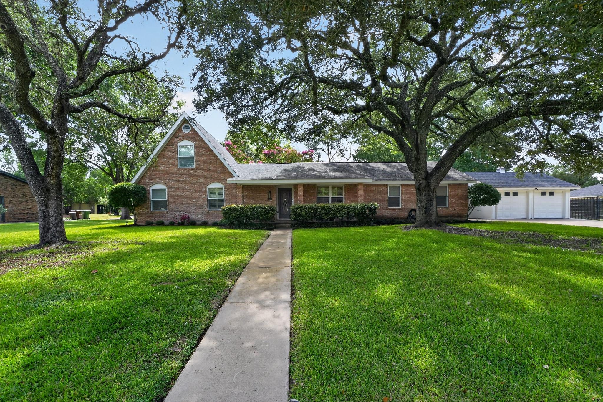 Mature trees shade a welcoming brick residence wi