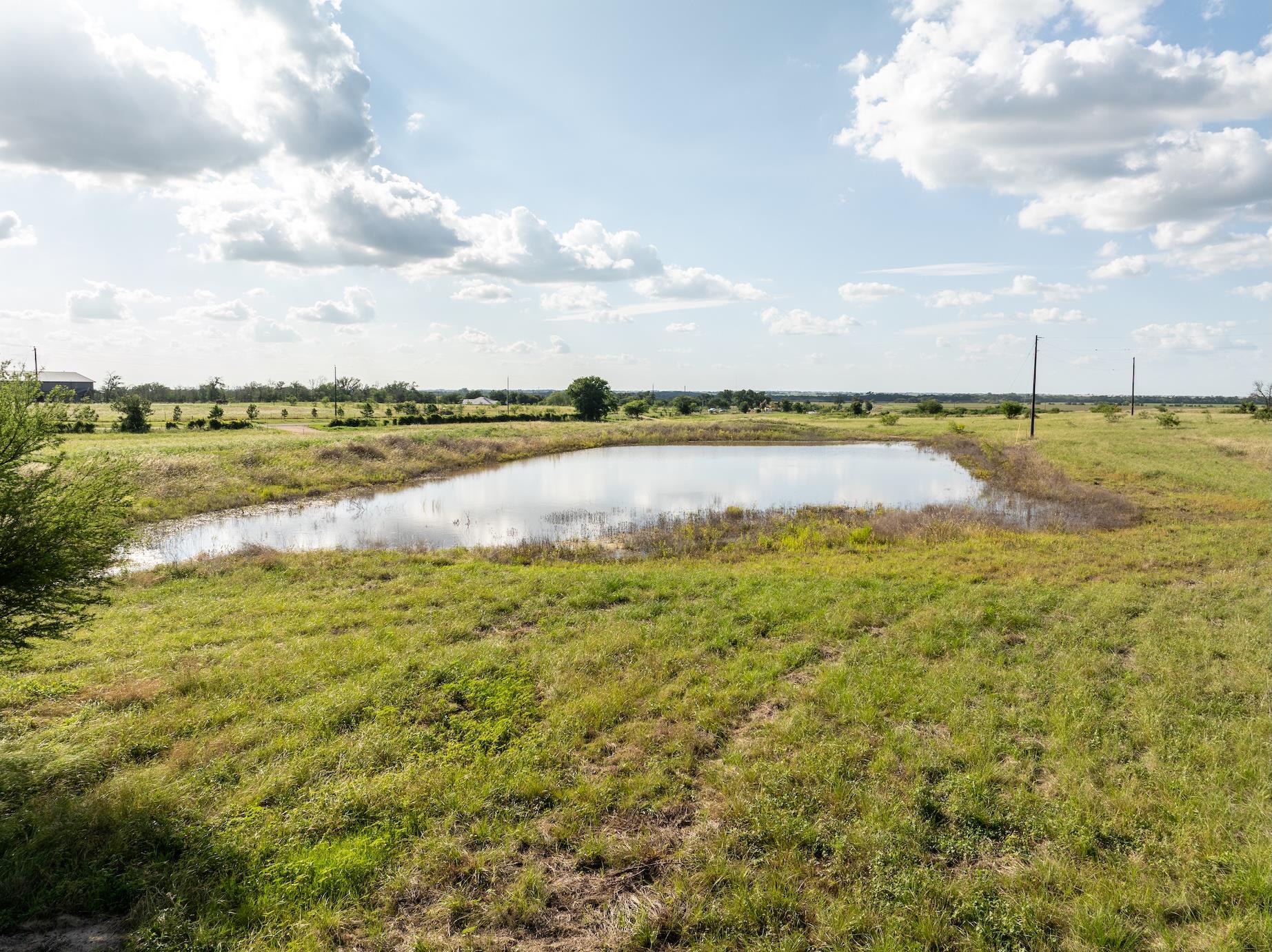 A tranquil pond glistens under a partly cloudy sk