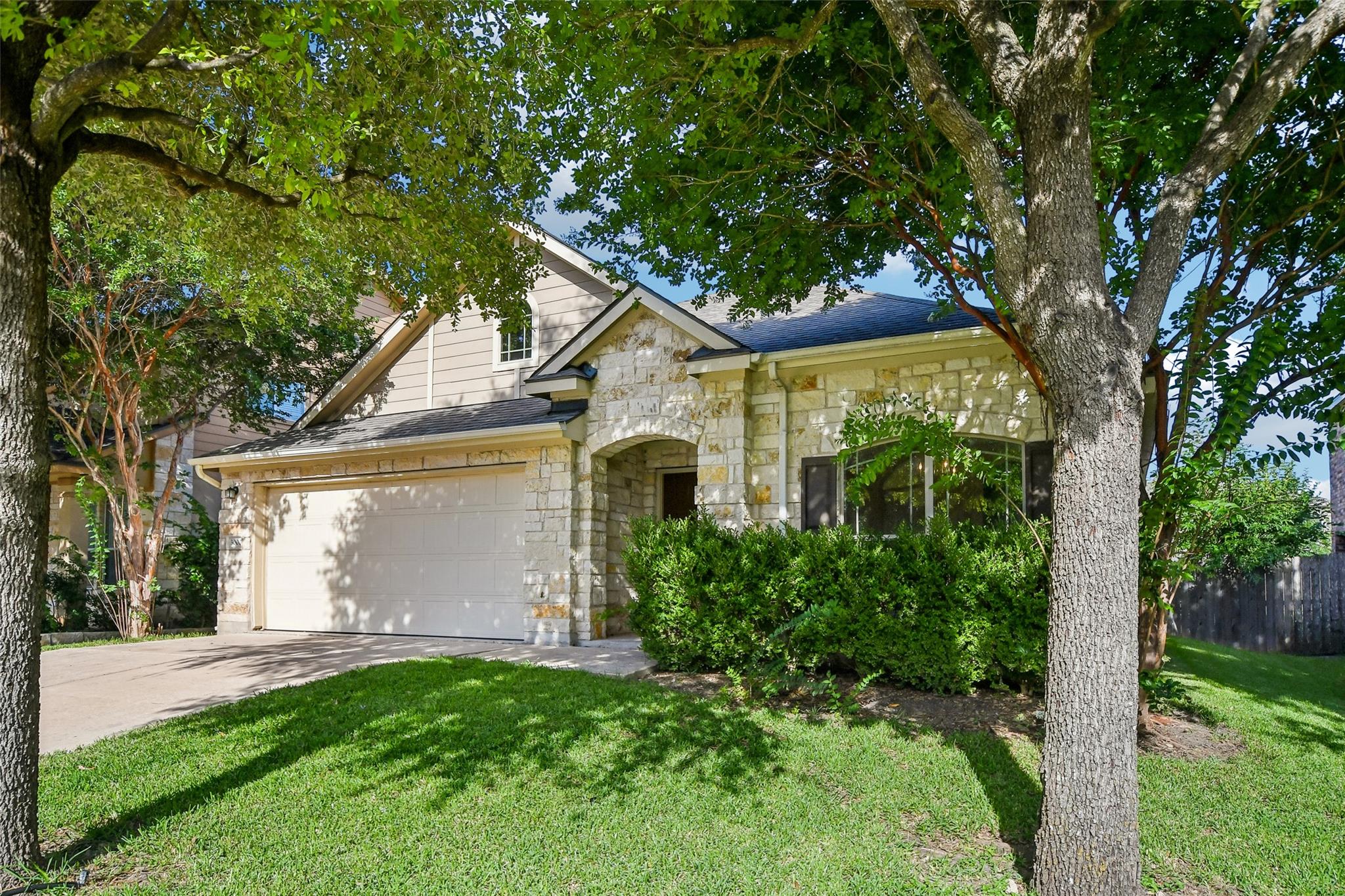 Mature trees frame a charming home with a stone a