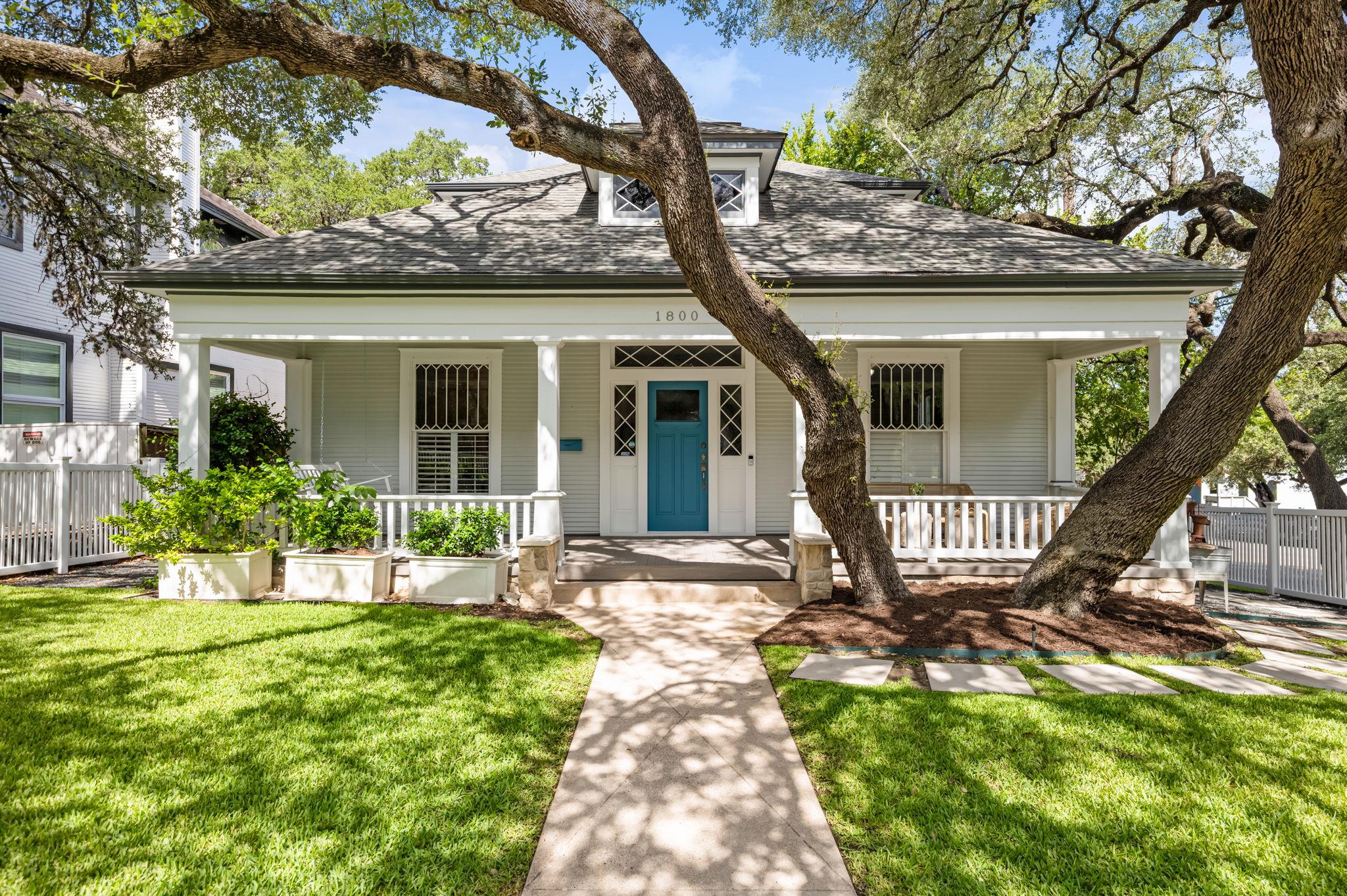 Mature shade trees frame a classic front porch wi