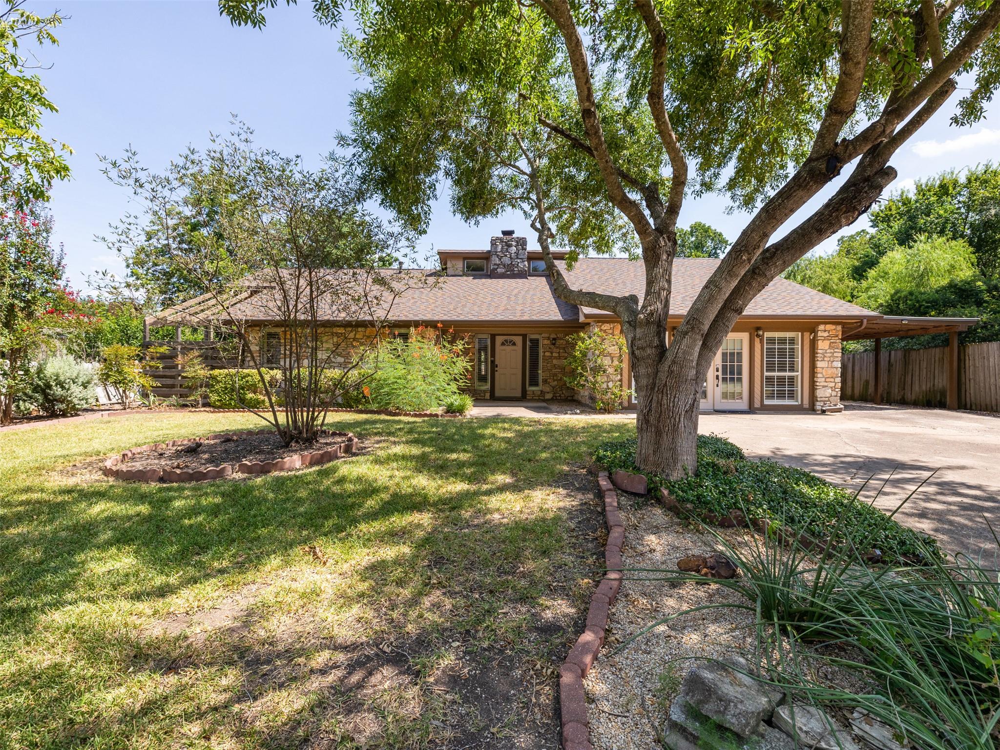 Mature trees frame a charming home with a stone a