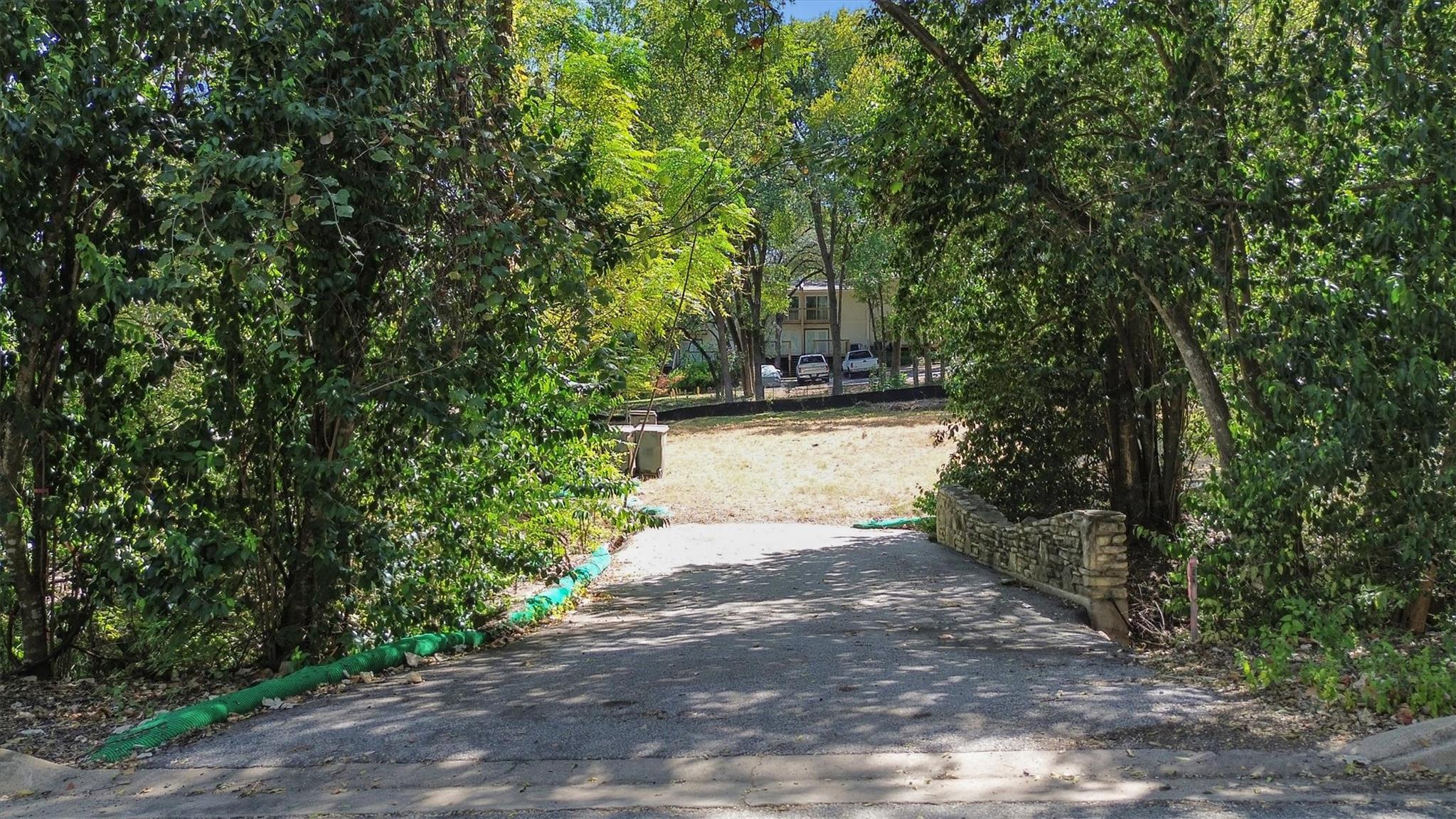 Mature trees frame the paved driveway leading tow