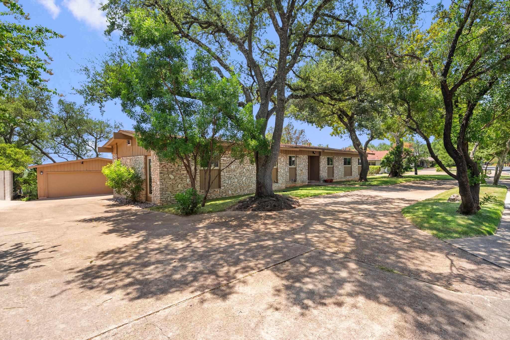 Mature trees shade the concrete driveway and ston