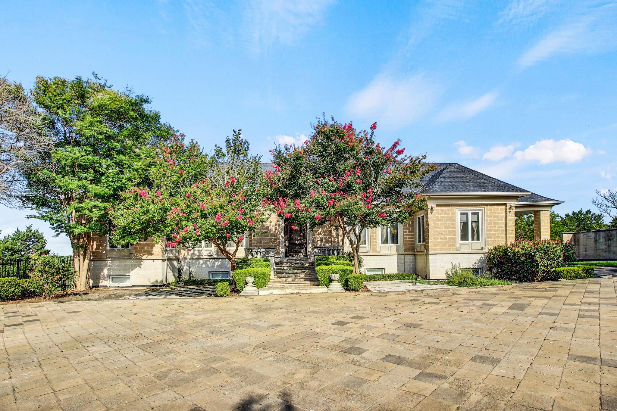 A grand paved driveway leads to a classic stone r