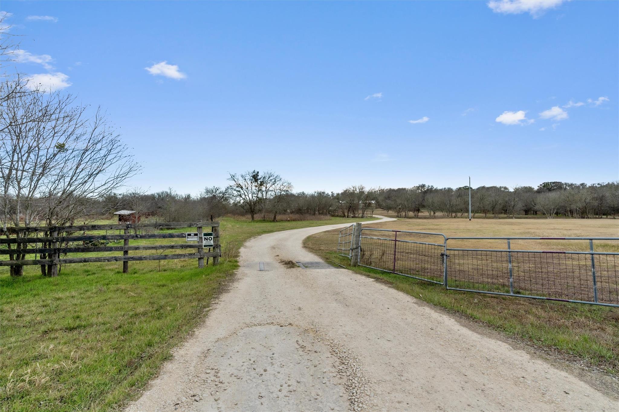 A long winding gravel driveway leads through open