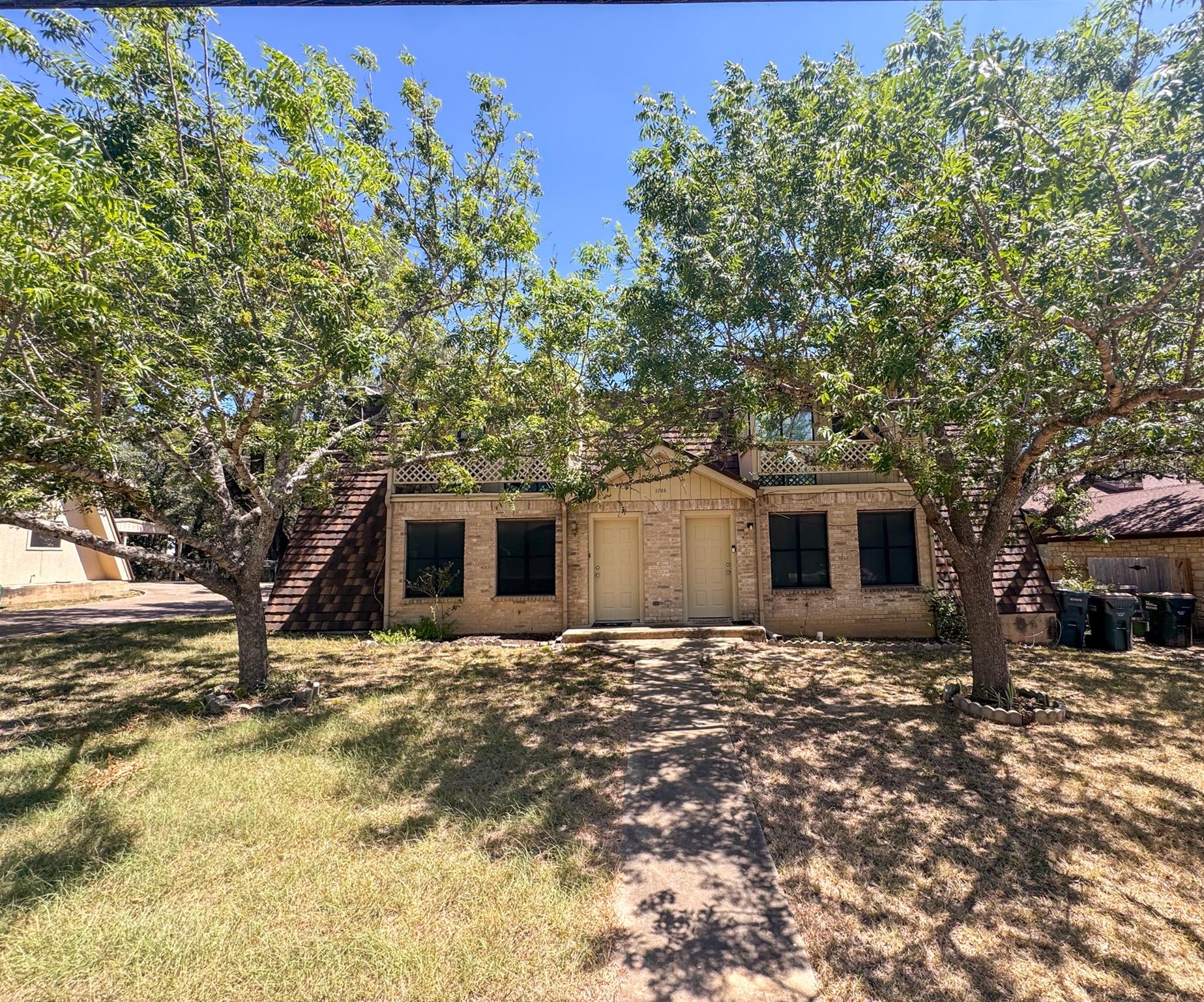 Mature trees shade the front lawn and paved concr