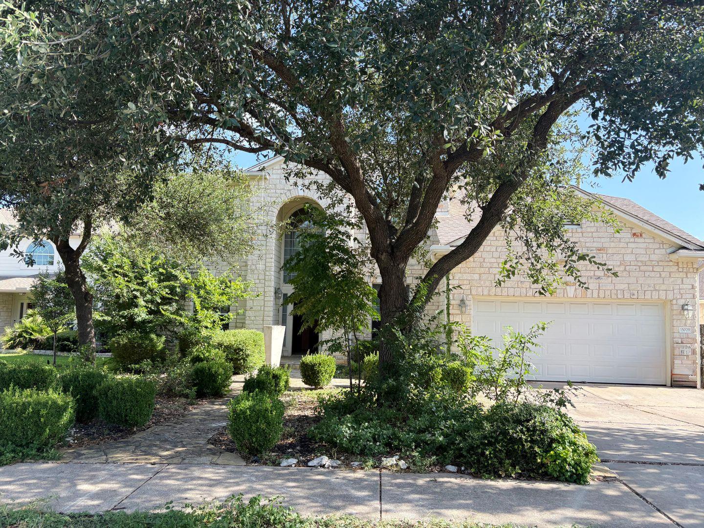 Mature trees shade the stone facade and paved dri