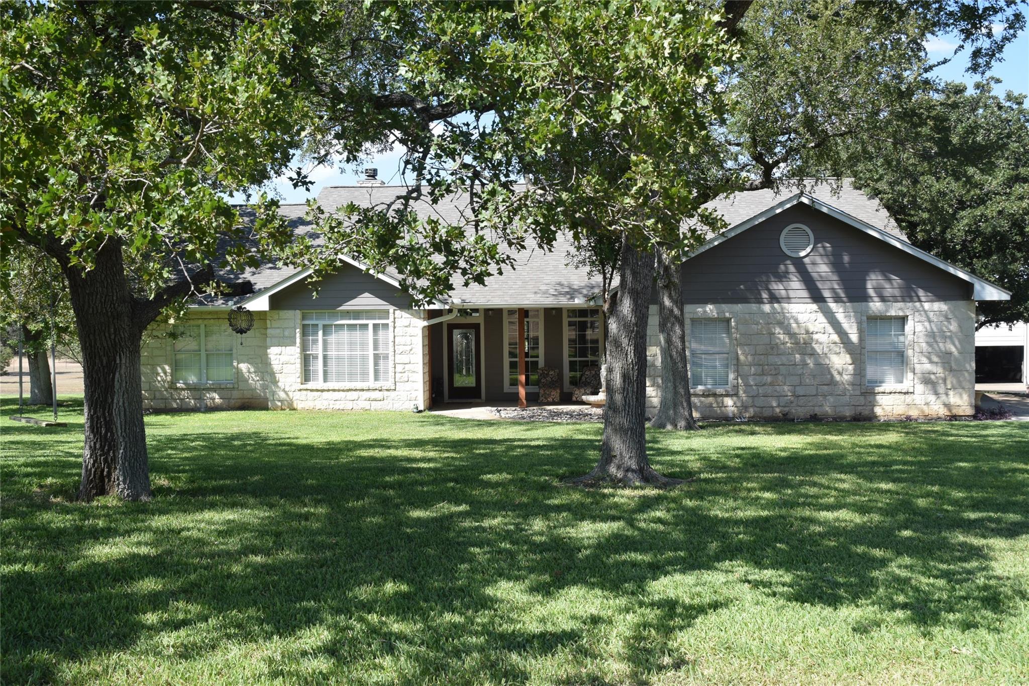 Mature trees shade the inviting stone and siding 