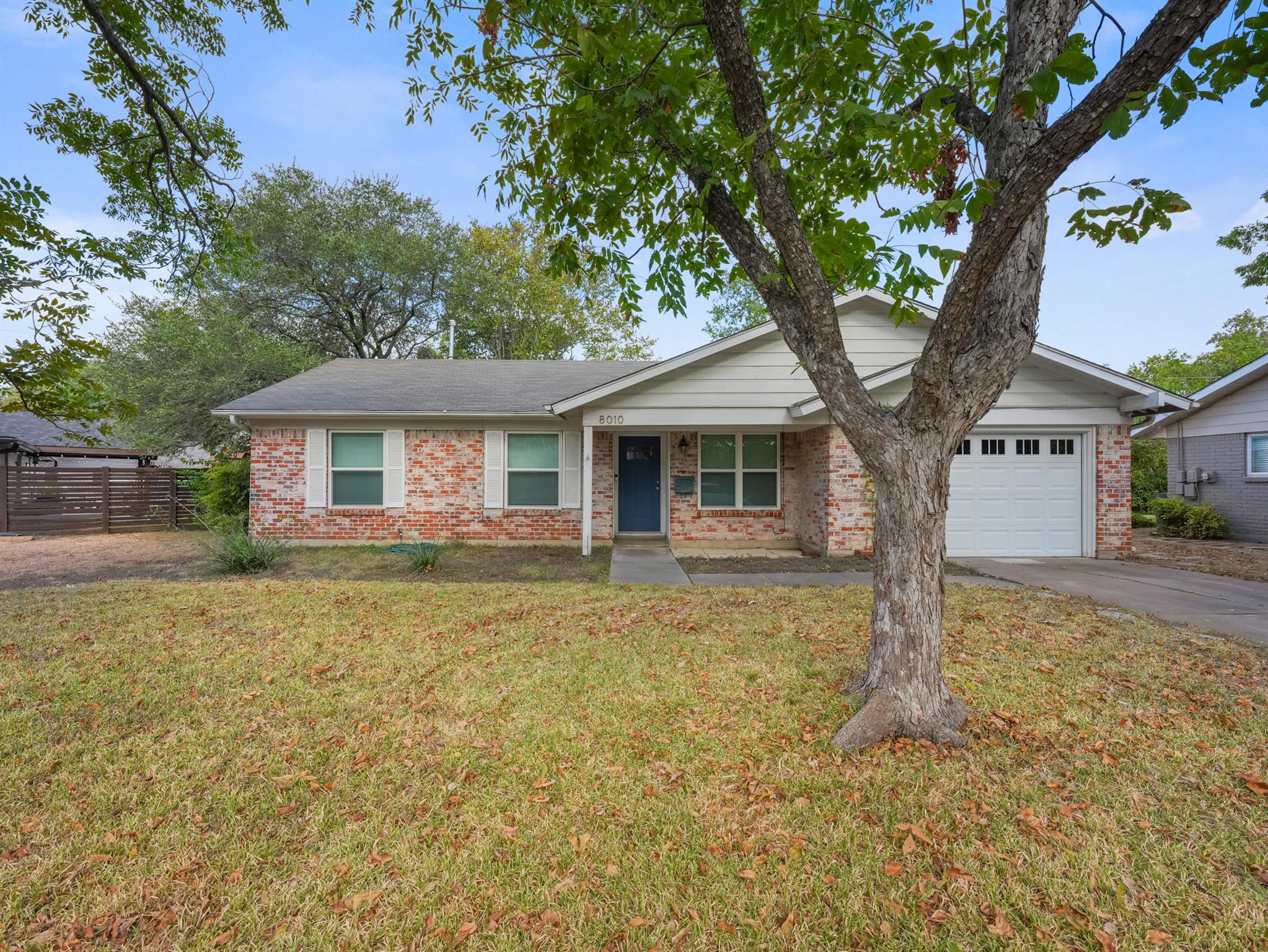 Mature trees frame this brick and siding single-s