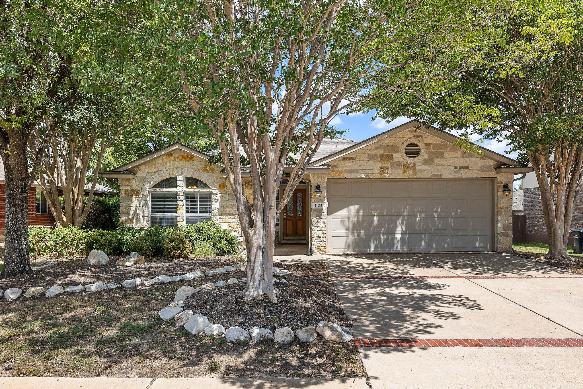 A charming stone facade with mature trees and an 