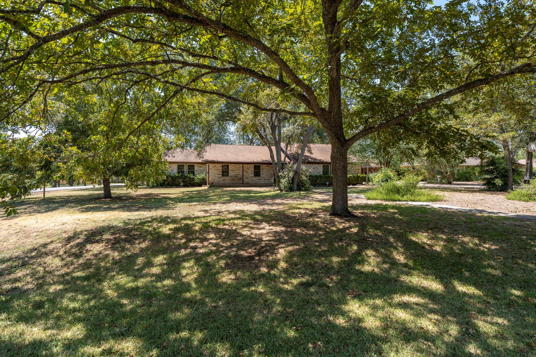 Mature shade trees frame the single-story stone e
