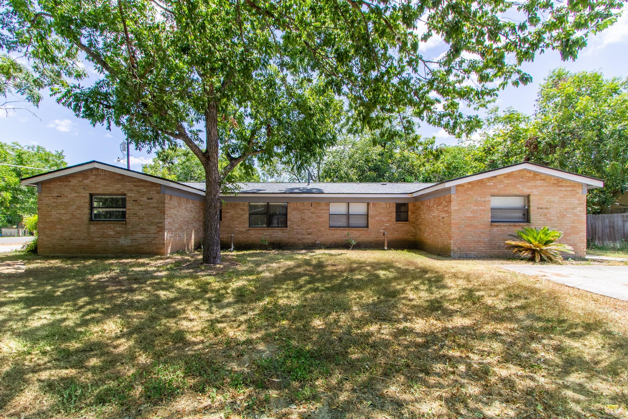 Mature shade trees frame the classic brick exteri