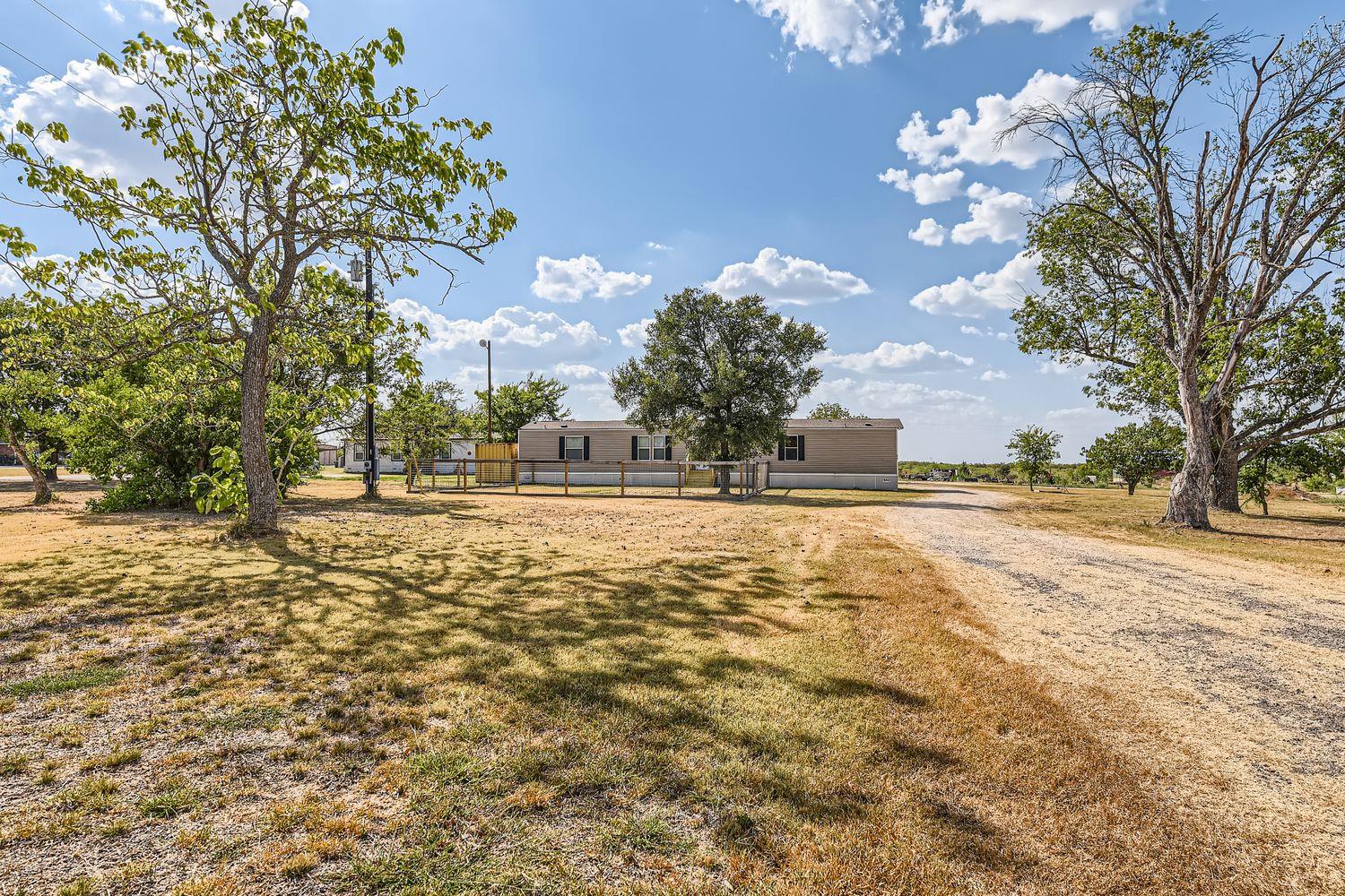 Mature trees shade a long driveway leading toward