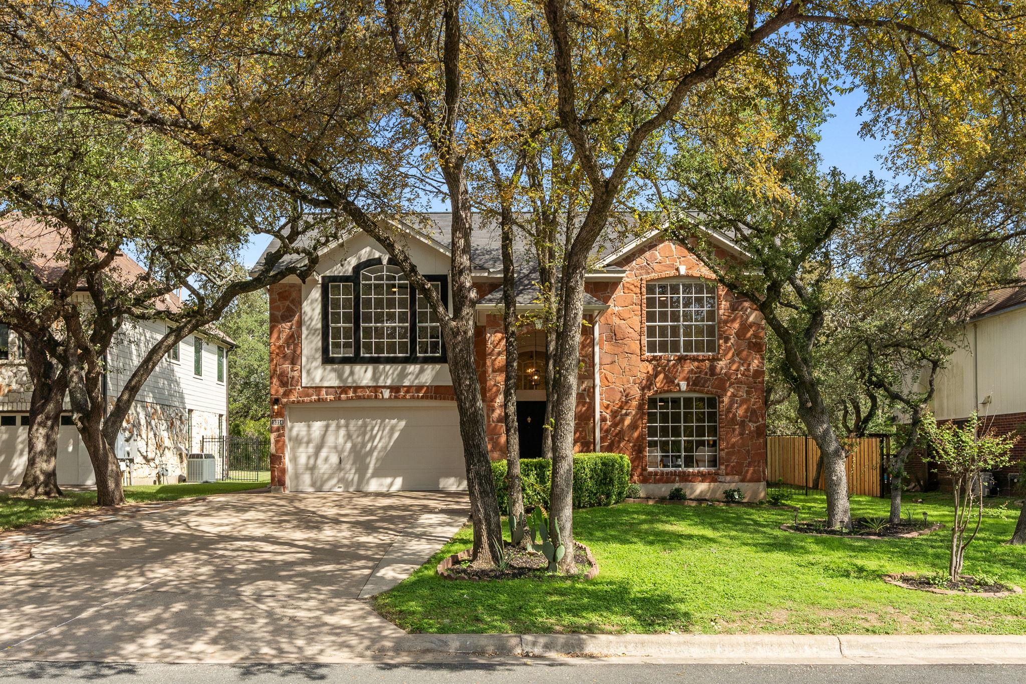 Mature trees frame a classic stone and siding ext