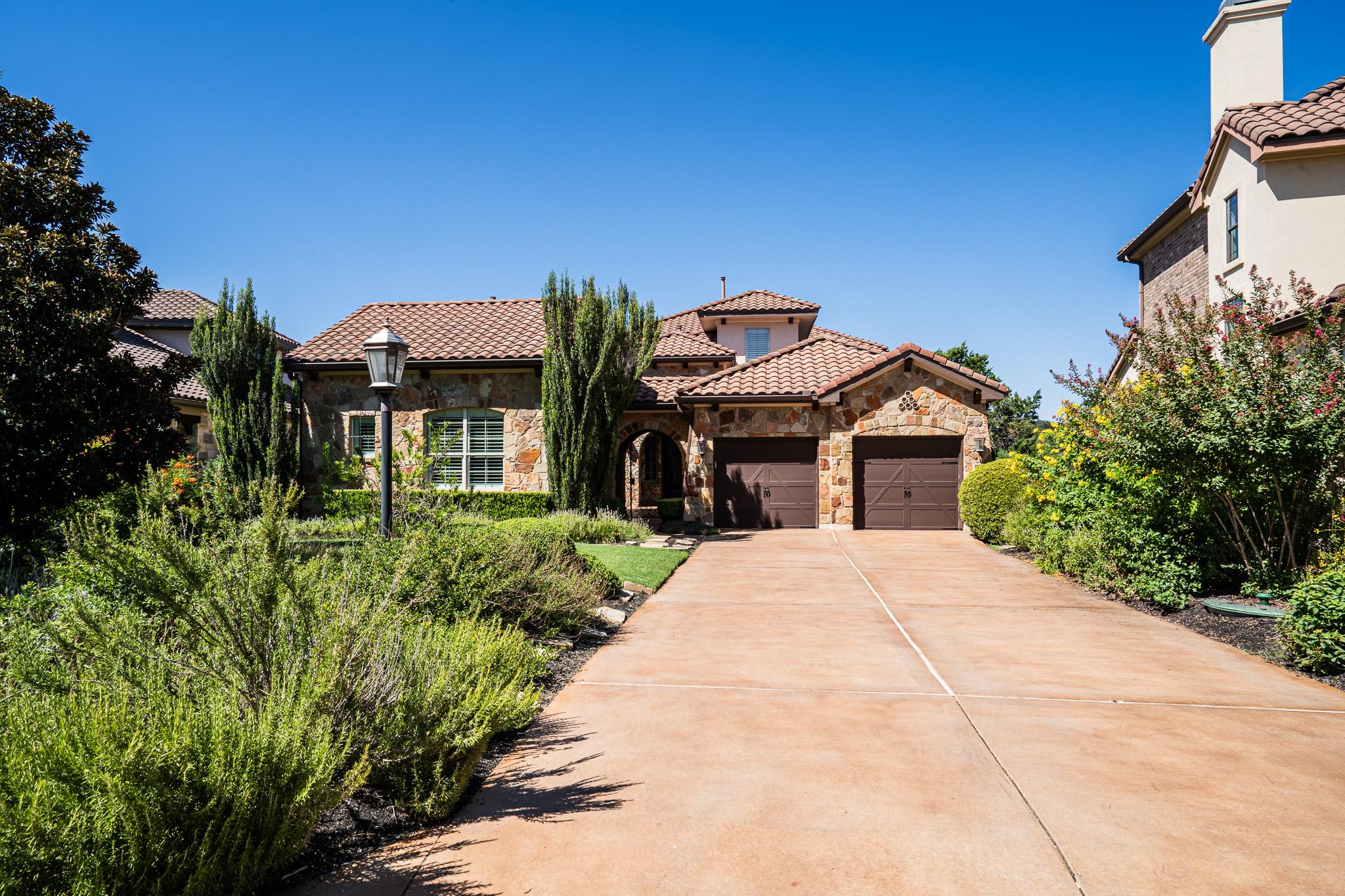 Textured stone siding and a warm concrete drivewa