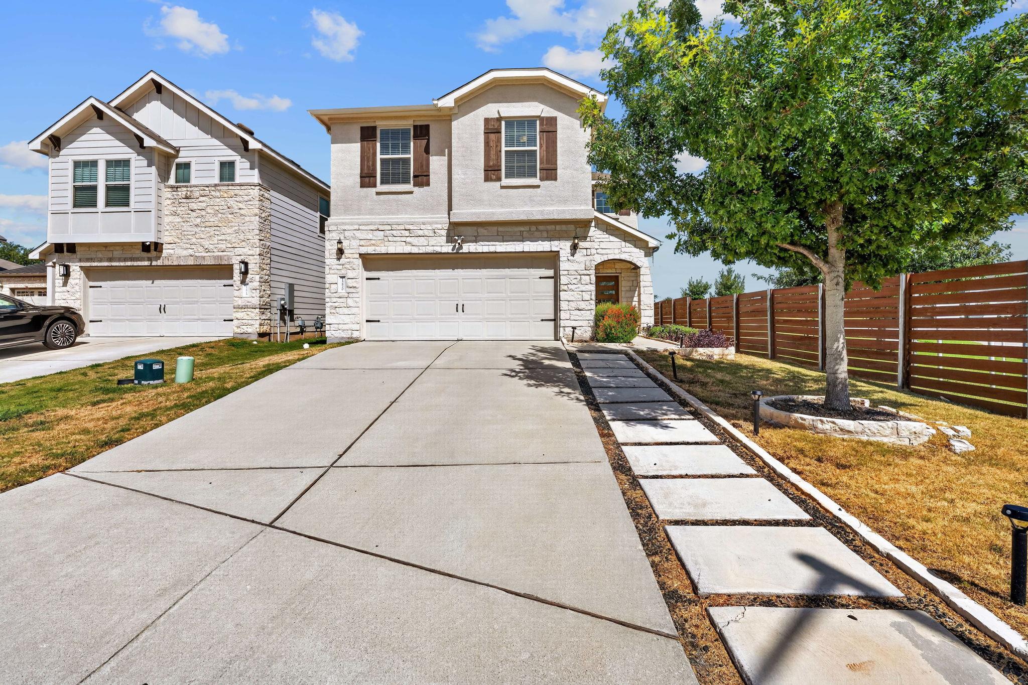 A concrete driveway leads to the two-story stone 