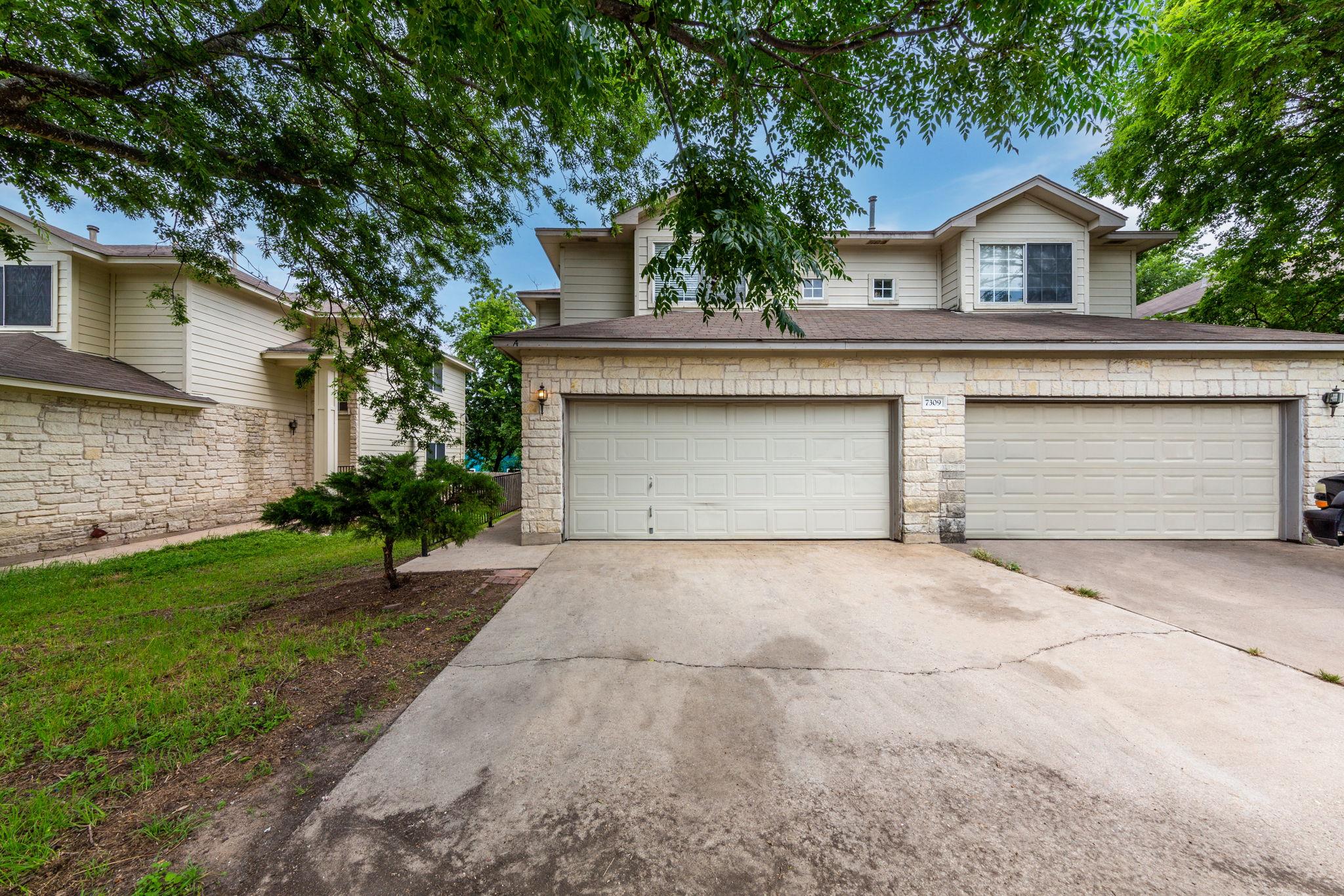 Mature trees shade the concrete driveway leading 