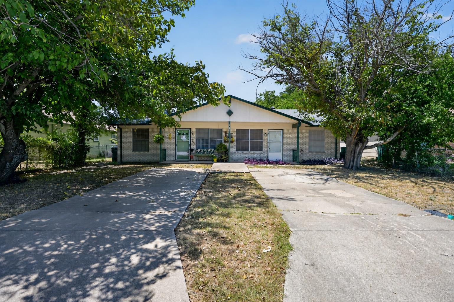 Mature shade trees flank dual driveways leading u