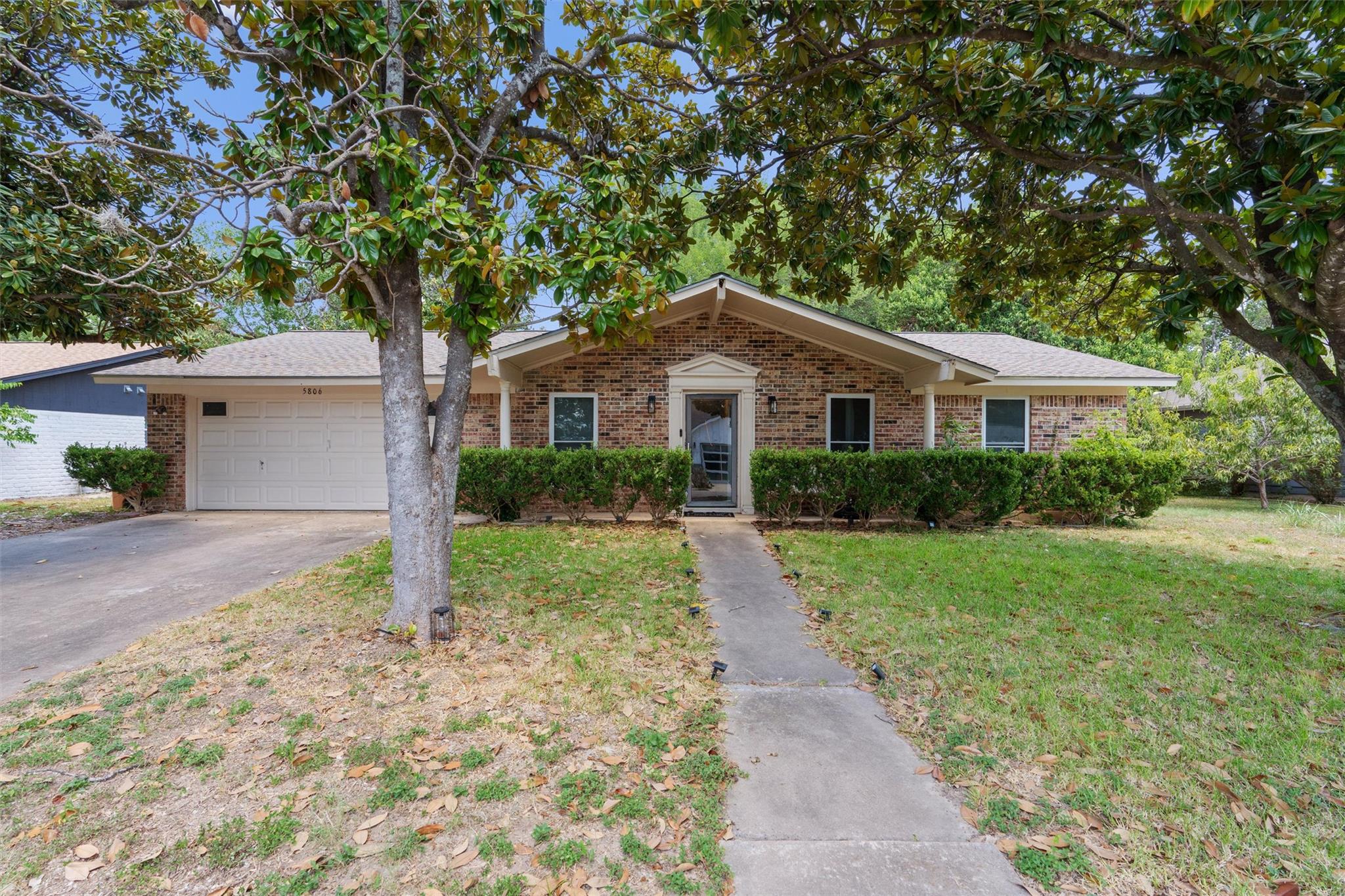 Mature trees shade a classic brick ranch facade f