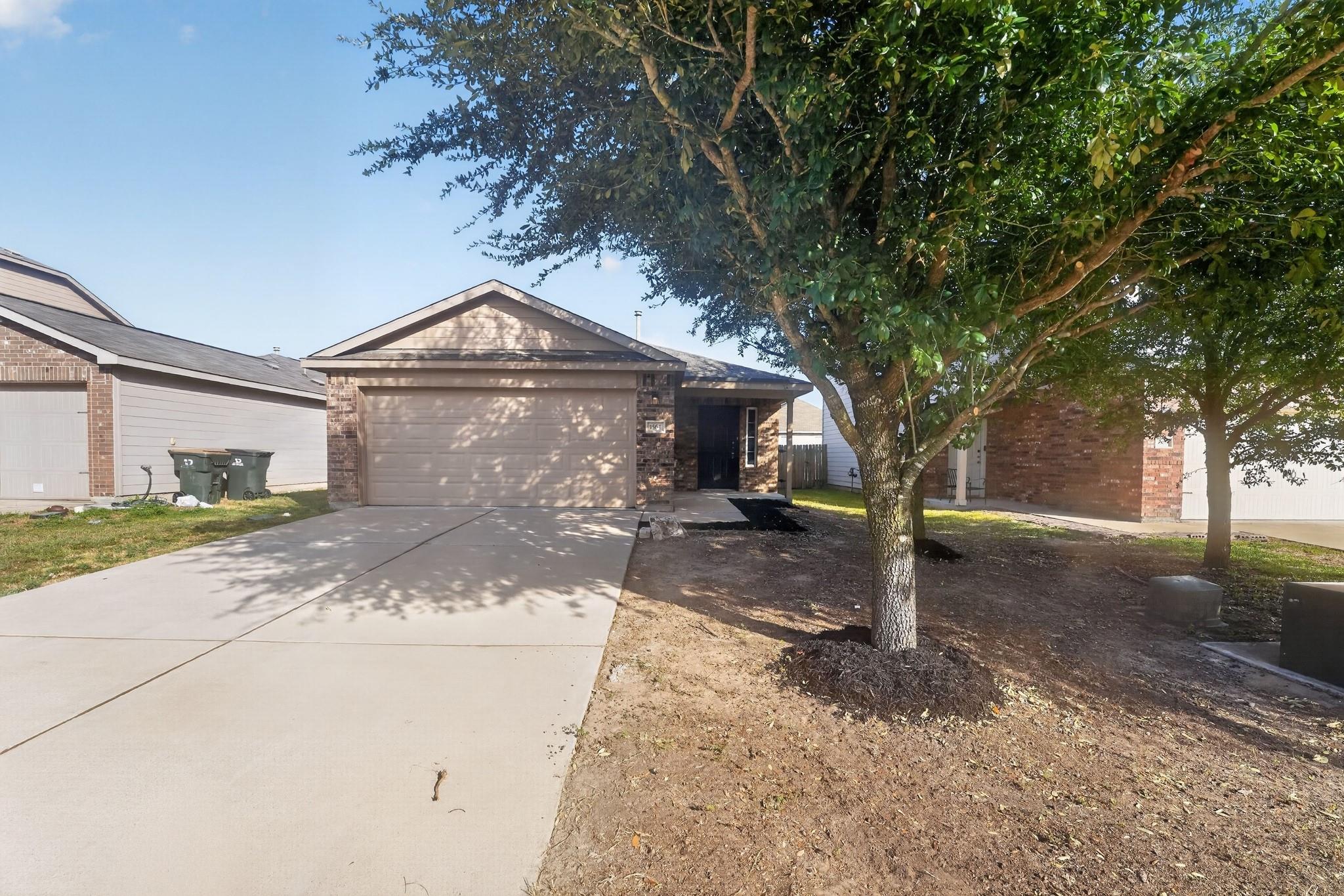 Mature trees shade a wide concrete driveway leadi