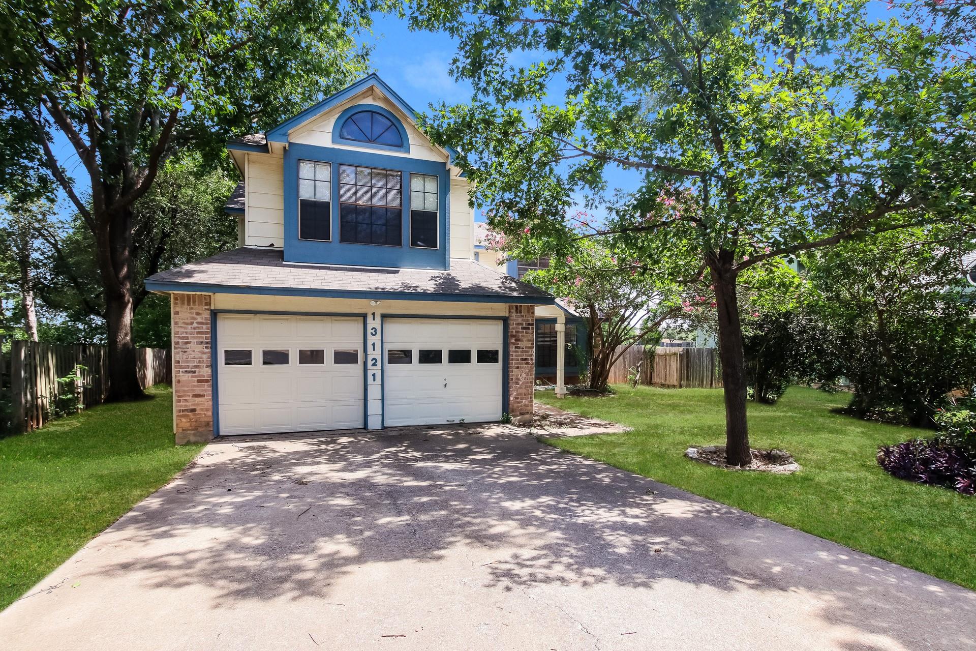 Mature trees frame a concrete driveway leading to