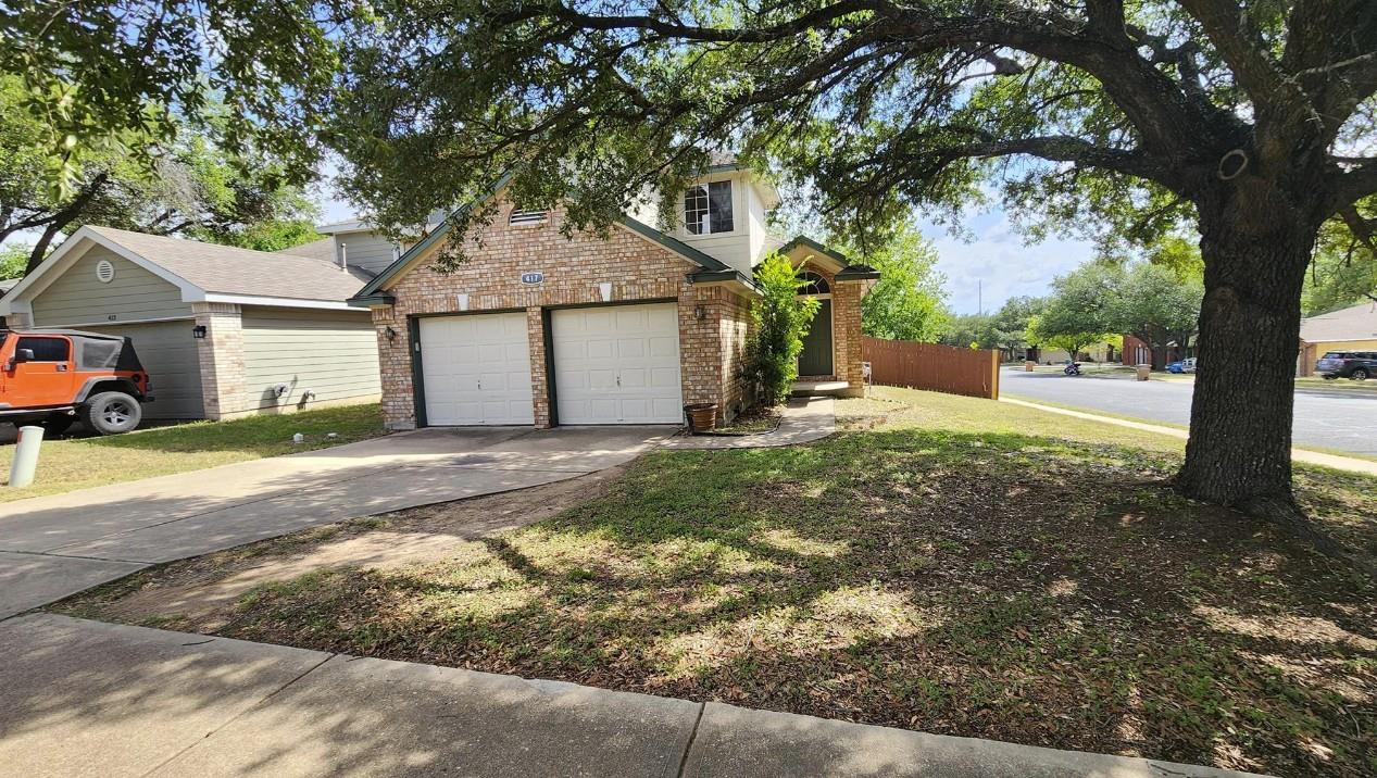 Mature shade trees and a concrete driveway lead t