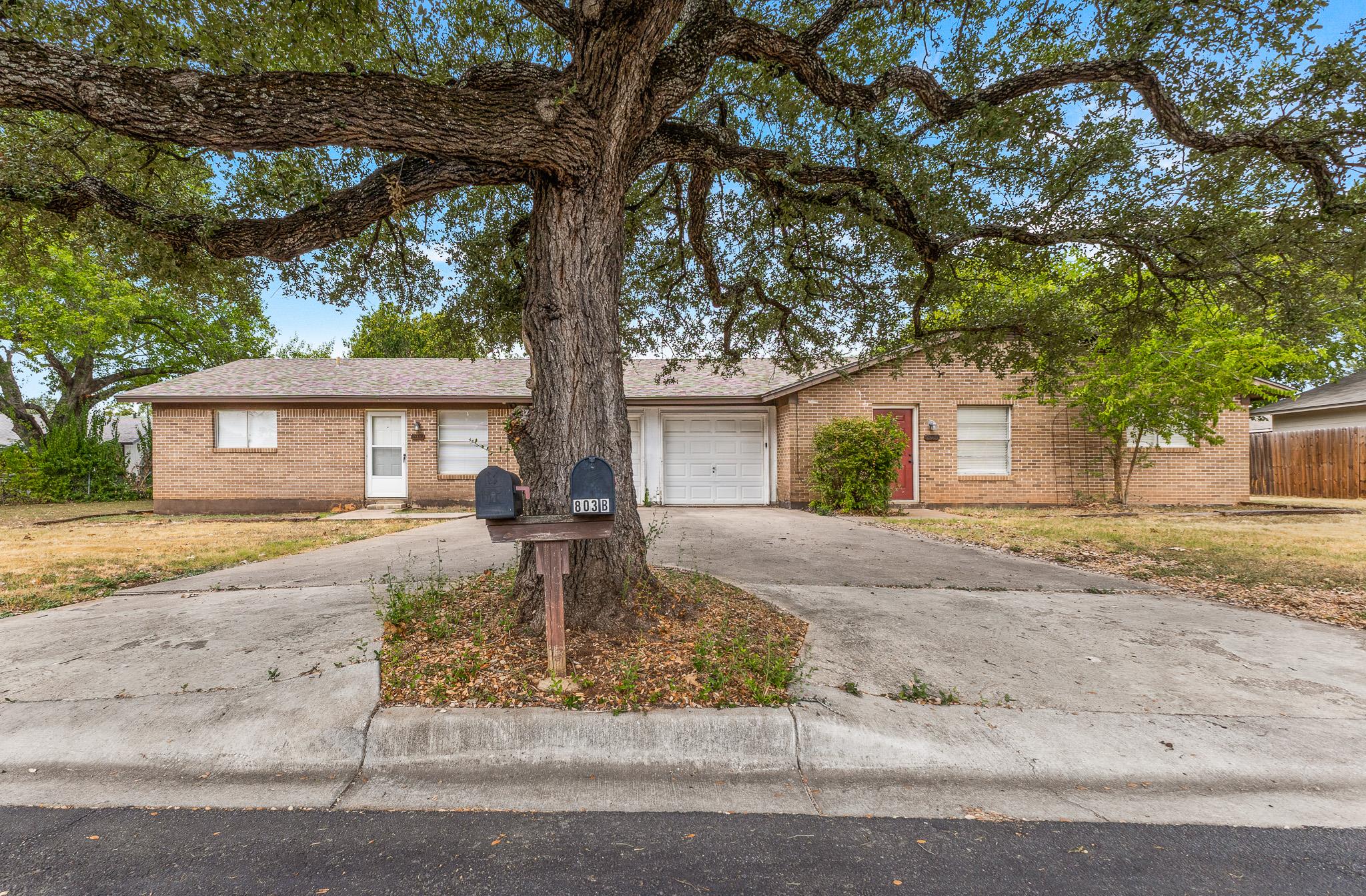 Mature oak trees shade a classic brick duplex fea