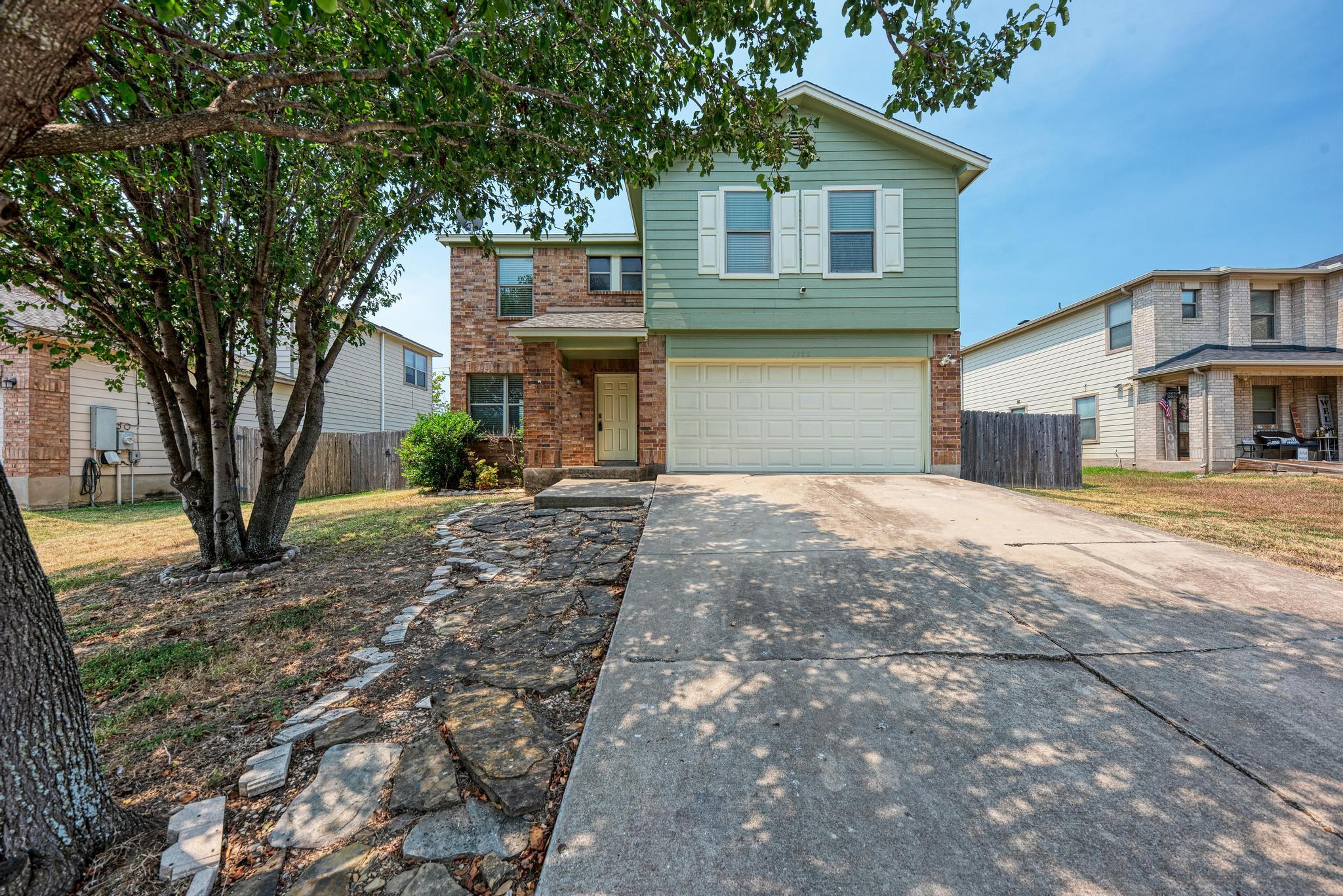 Mature trees shade a wide concrete driveway leadi