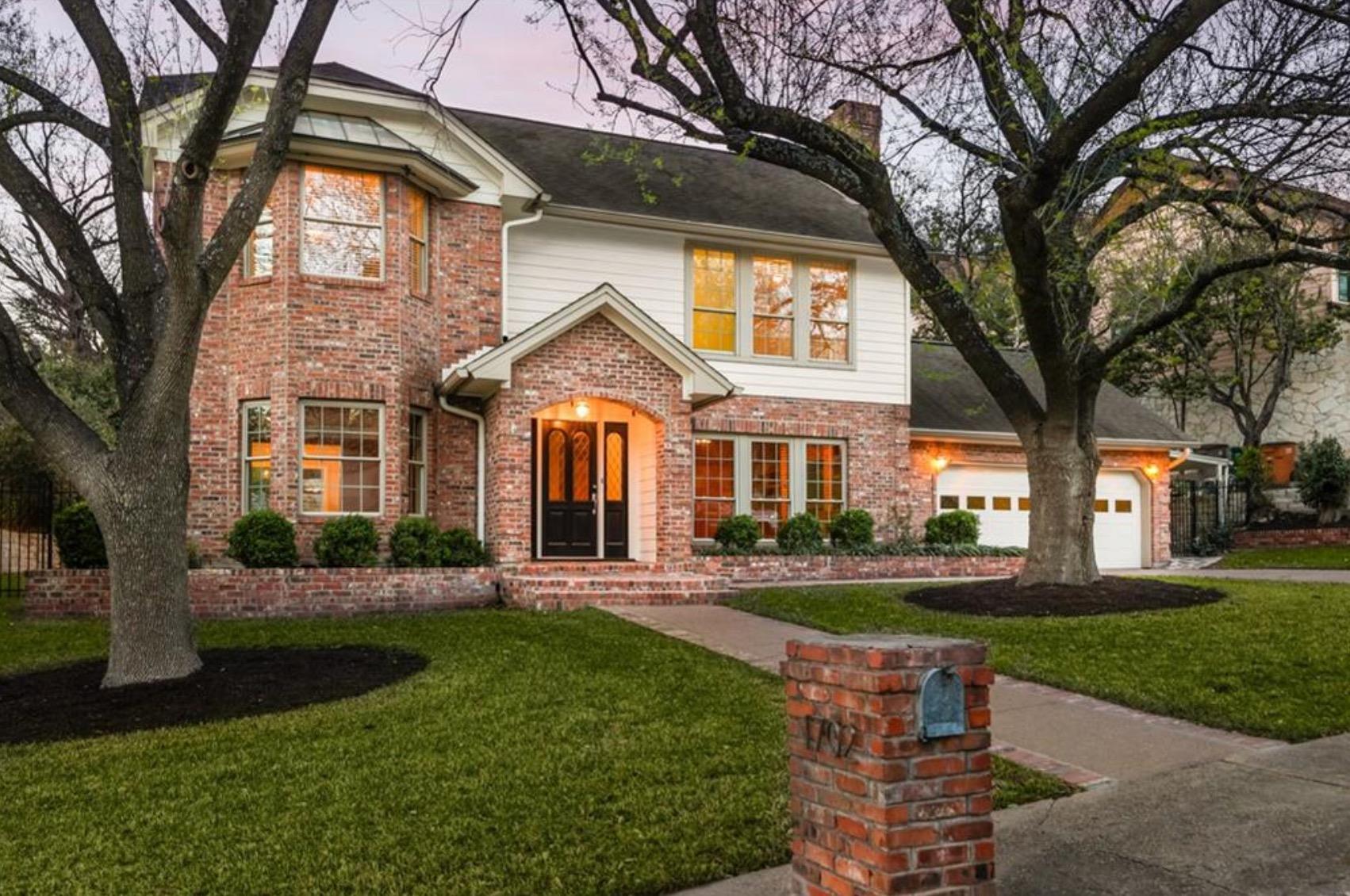 Mature trees shade a classic brick and siding fac