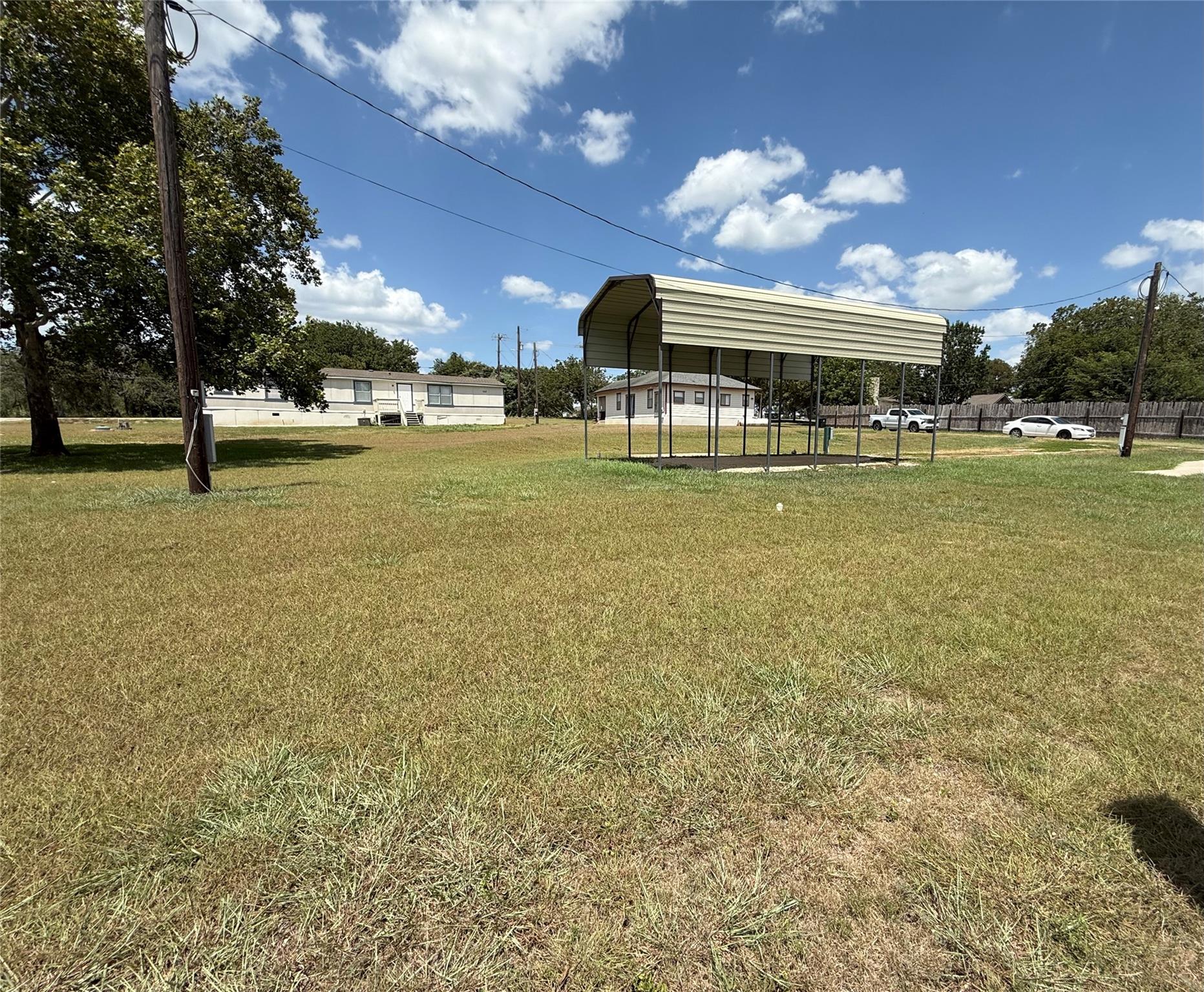 An open grassy yard features a metal carport unde