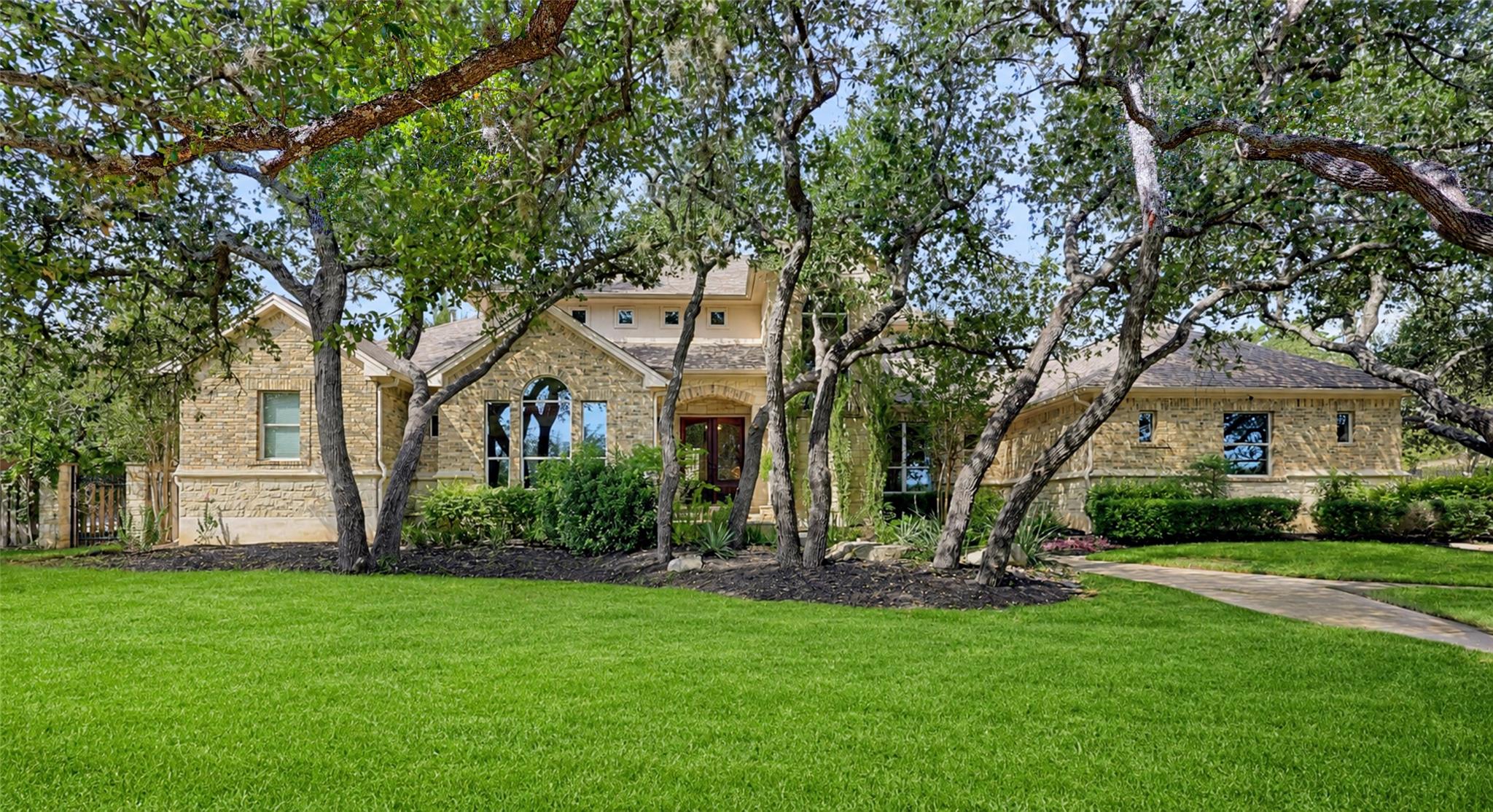 Mature oak trees frame a stone facade on a manicu