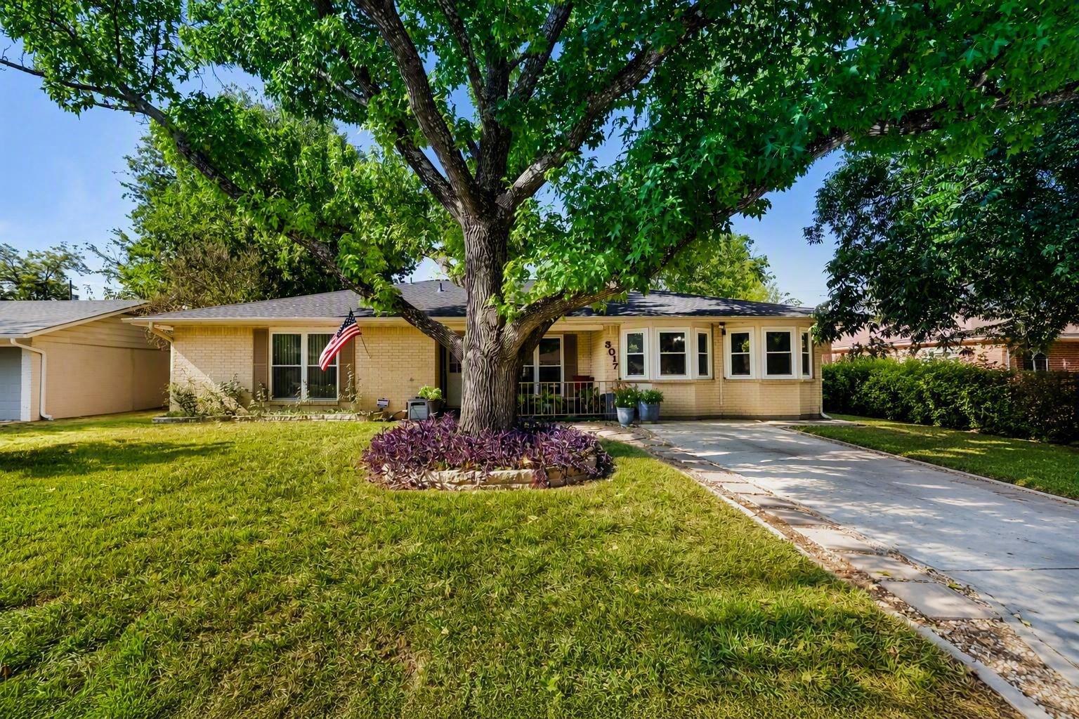 Mature shade trees frame the classic brick exteri