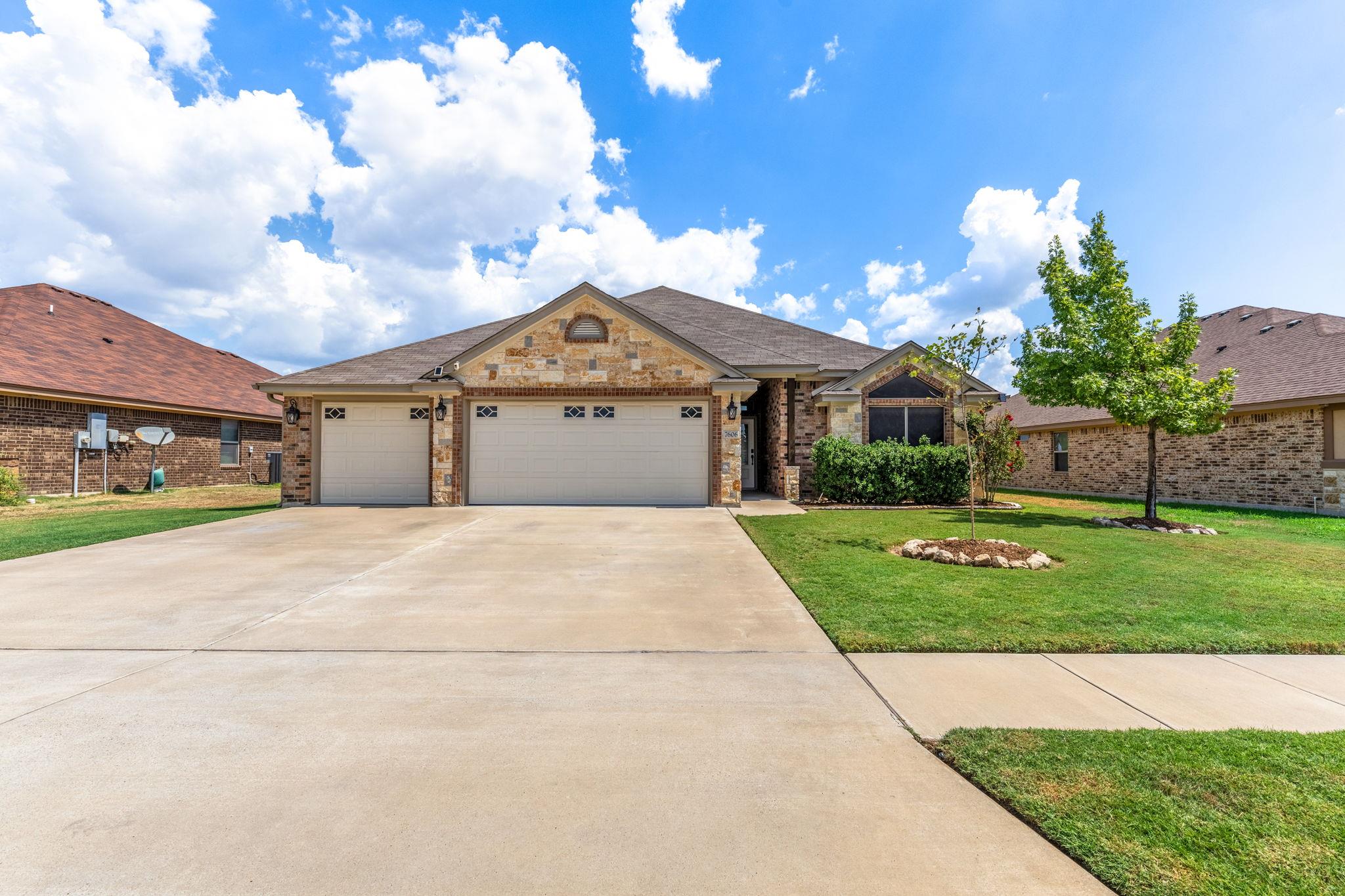 A spacious concrete driveway leads to this stone-