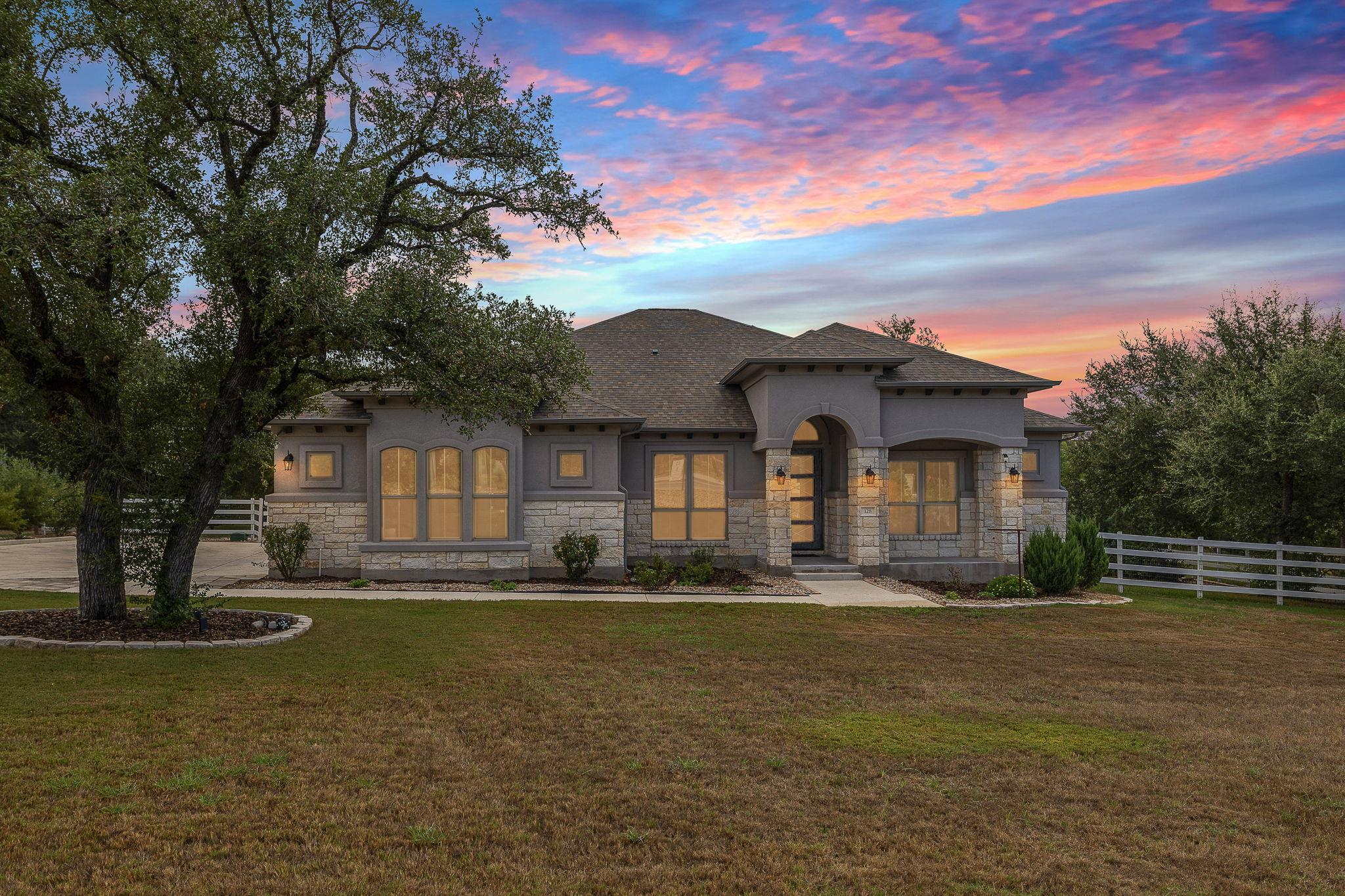 Mature trees frame a single-story stone and stucc