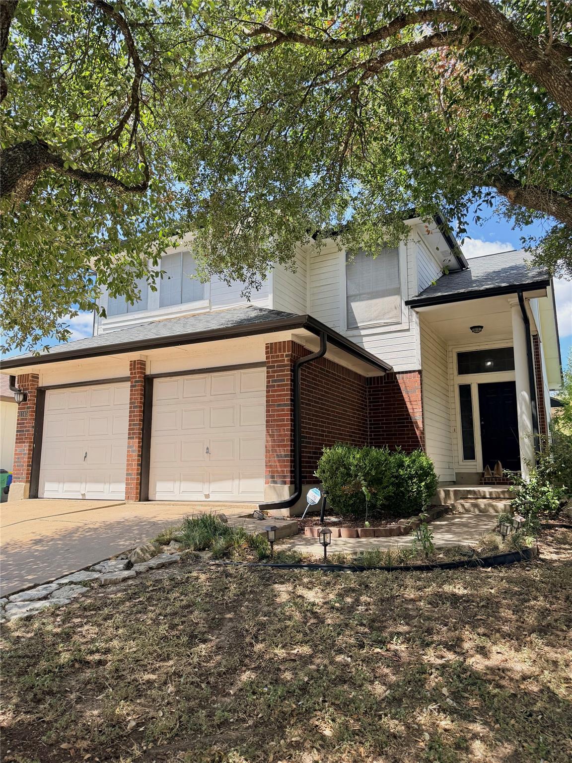 Mature trees shade a classic brick and siding fac